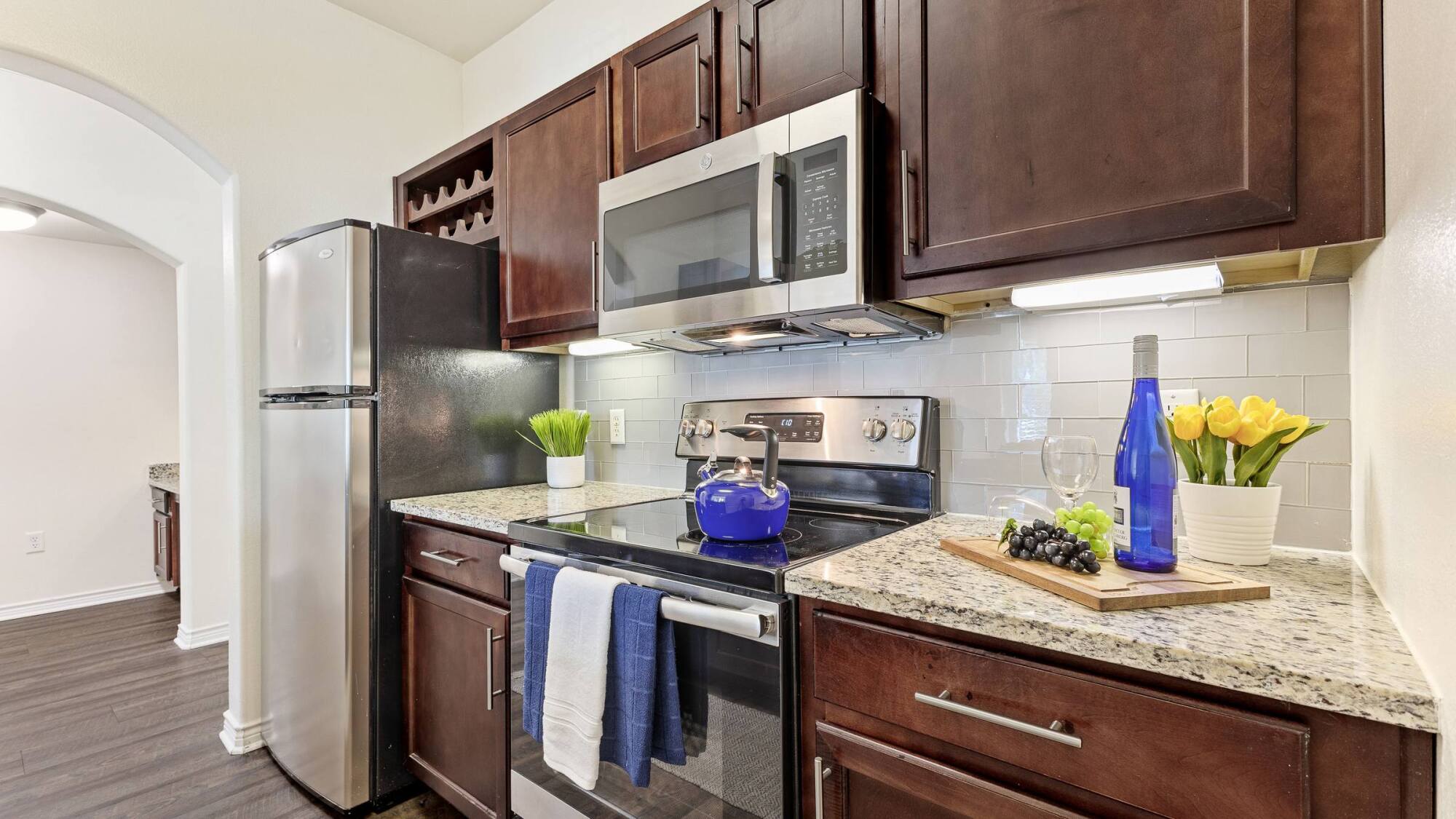 Modern kitchen with dark wood cabinets, stainless steel appliances, and a counter with wine, grapes, and yellow tulips.