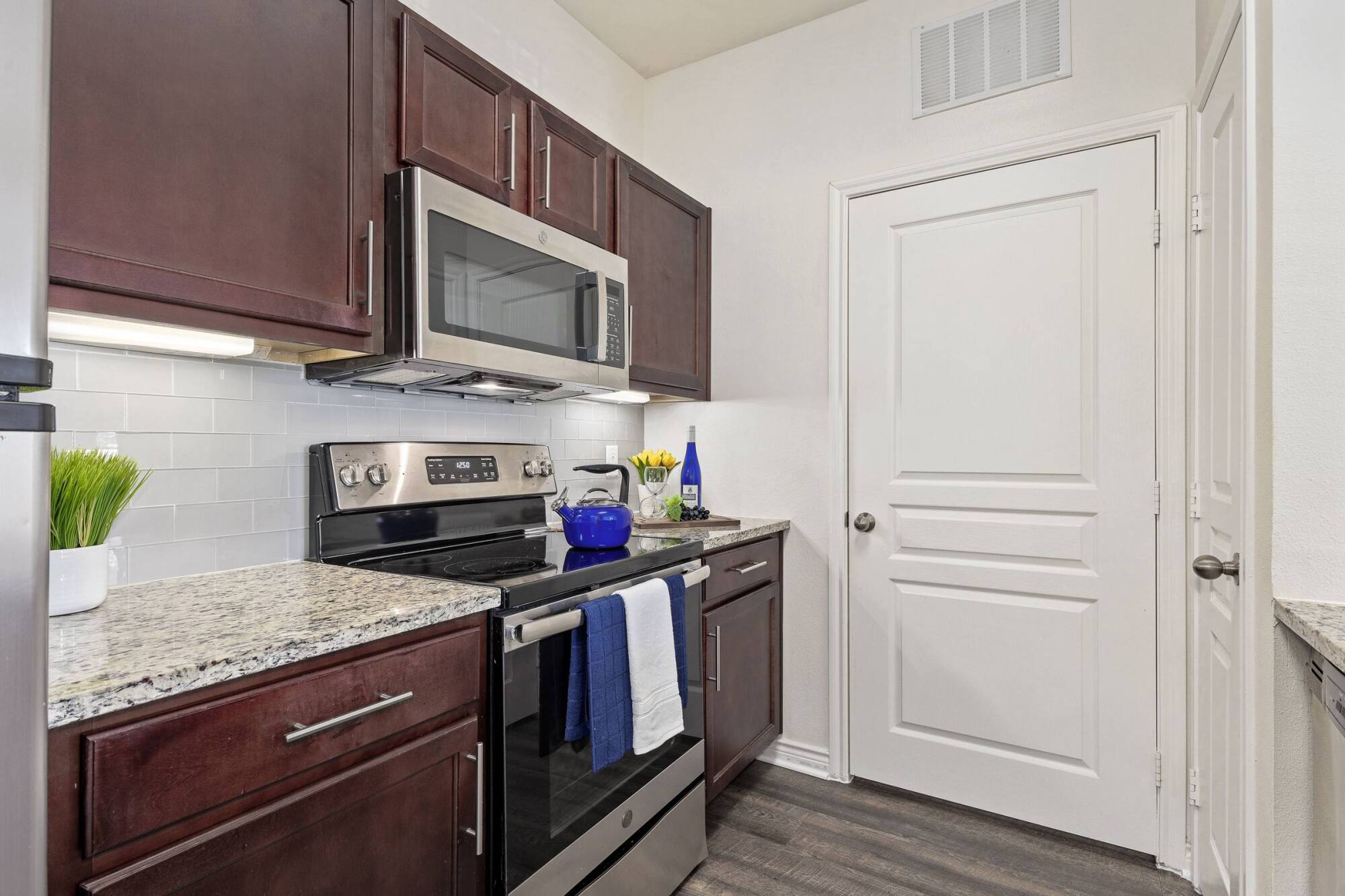 Modern kitchen with dark wood cabinets, stainless steel appliances, granite countertops, and white tile backsplash.
