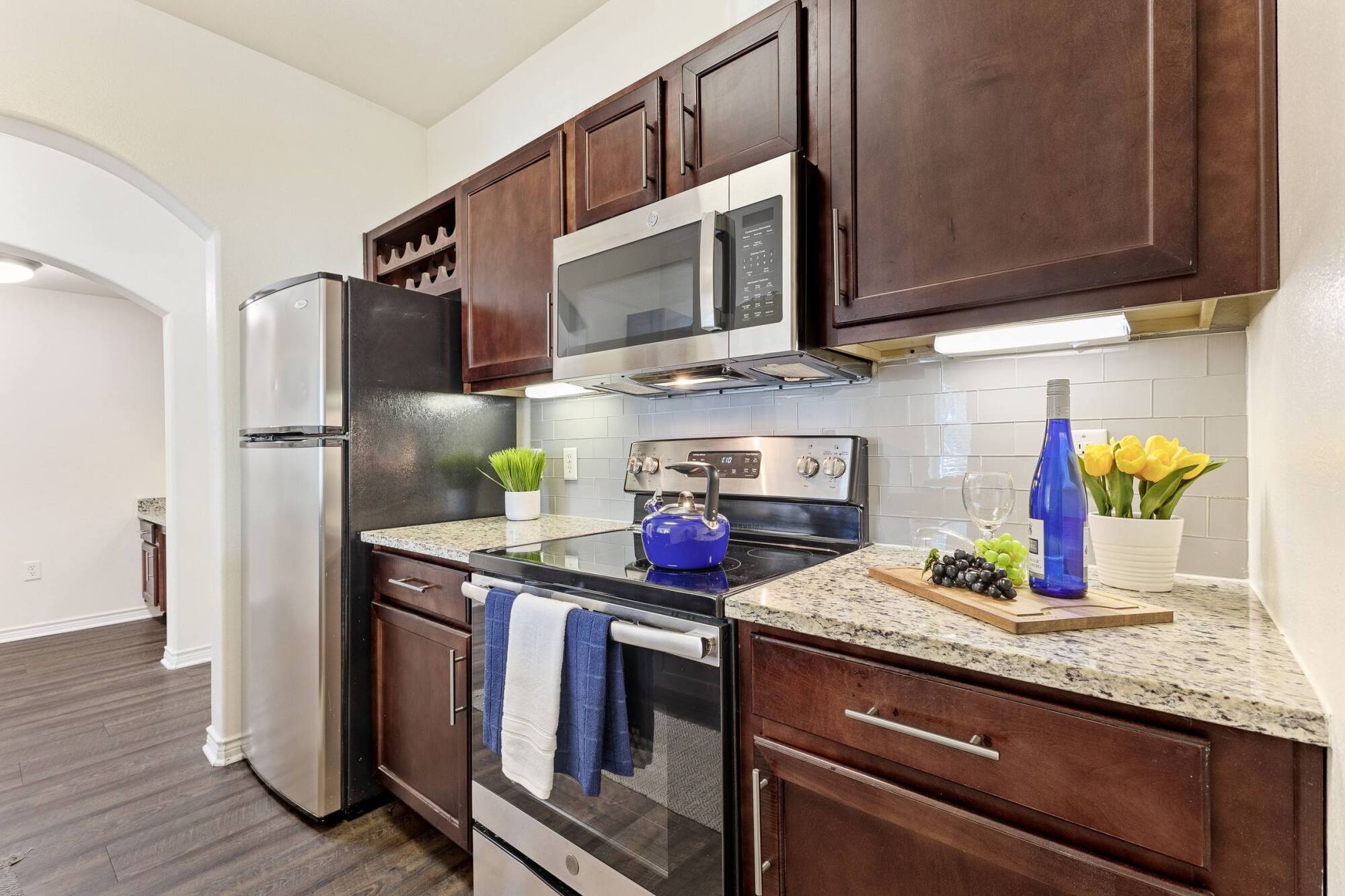 Modern kitchen with dark cabinets, stainless steel appliances, and a counter with wine, grapes, and flowers.