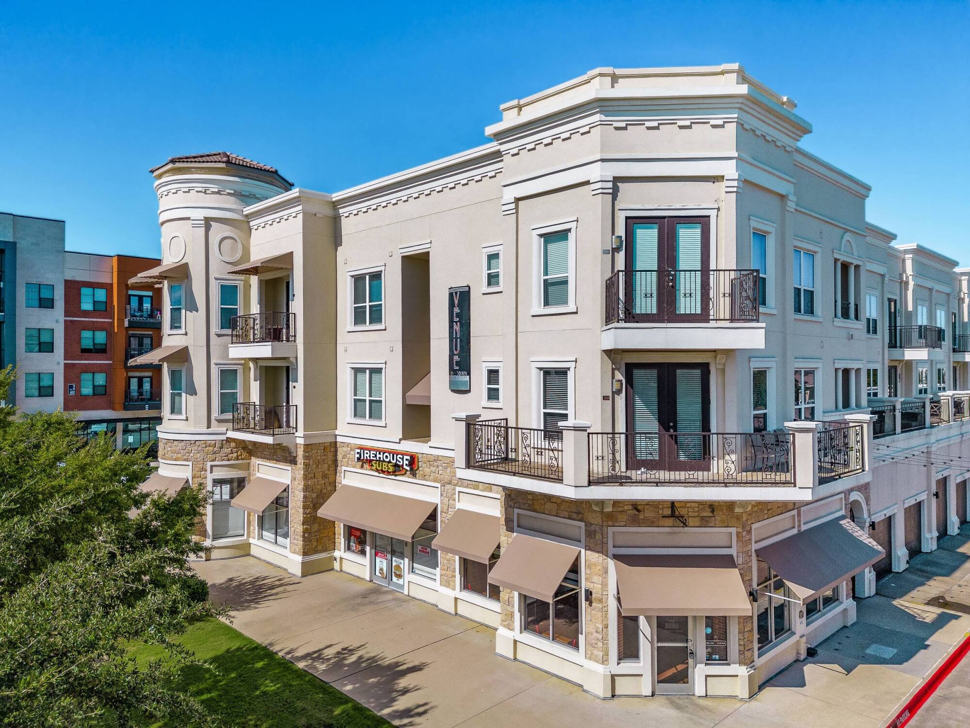 Corner view of a modern three-story building with retail shops and apartments, under a clear blue sky.