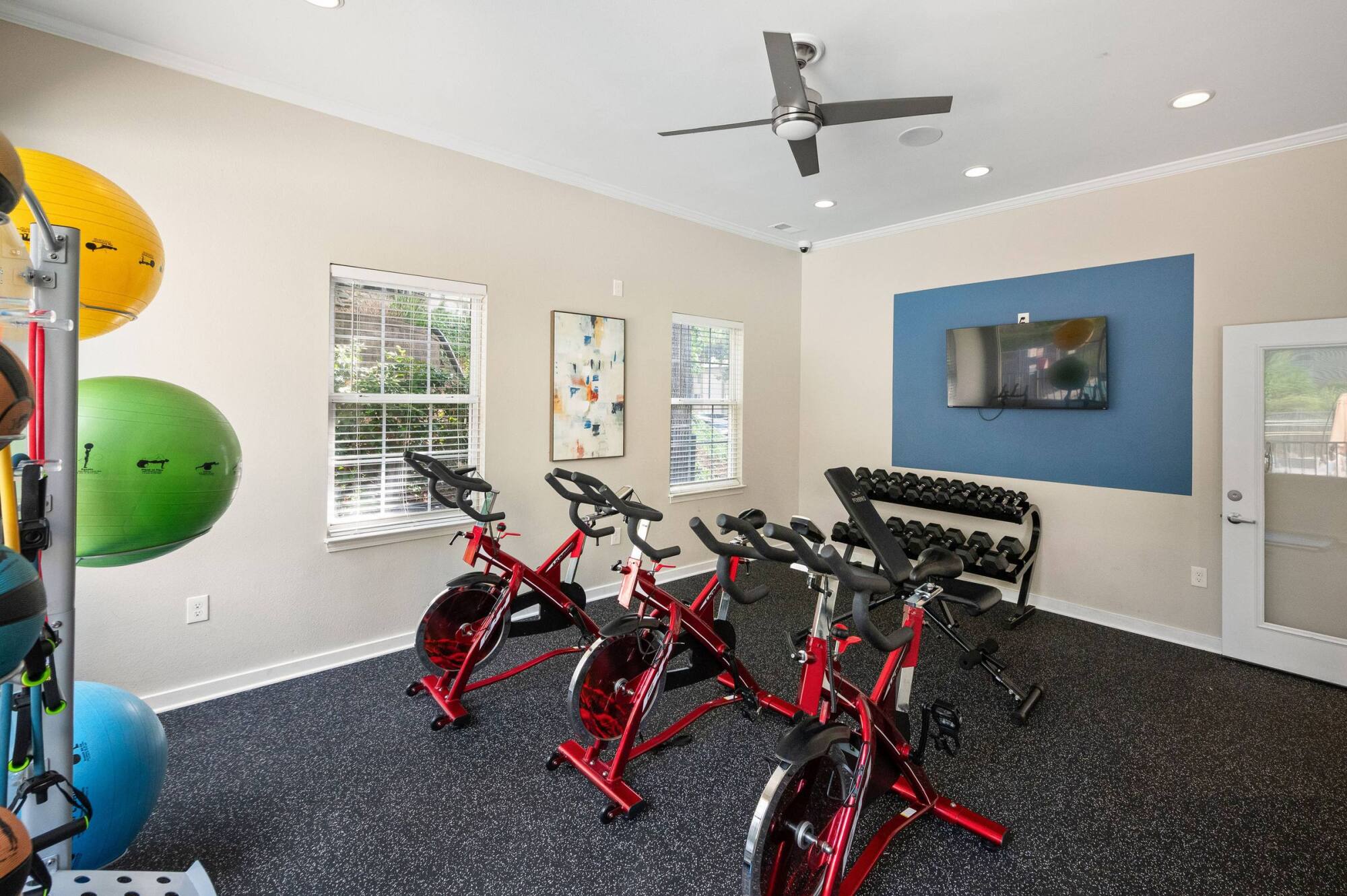 Spin studio at The Whitney with three indoor cycling bikes, a dumbbell rack, and a wall-mounted television.