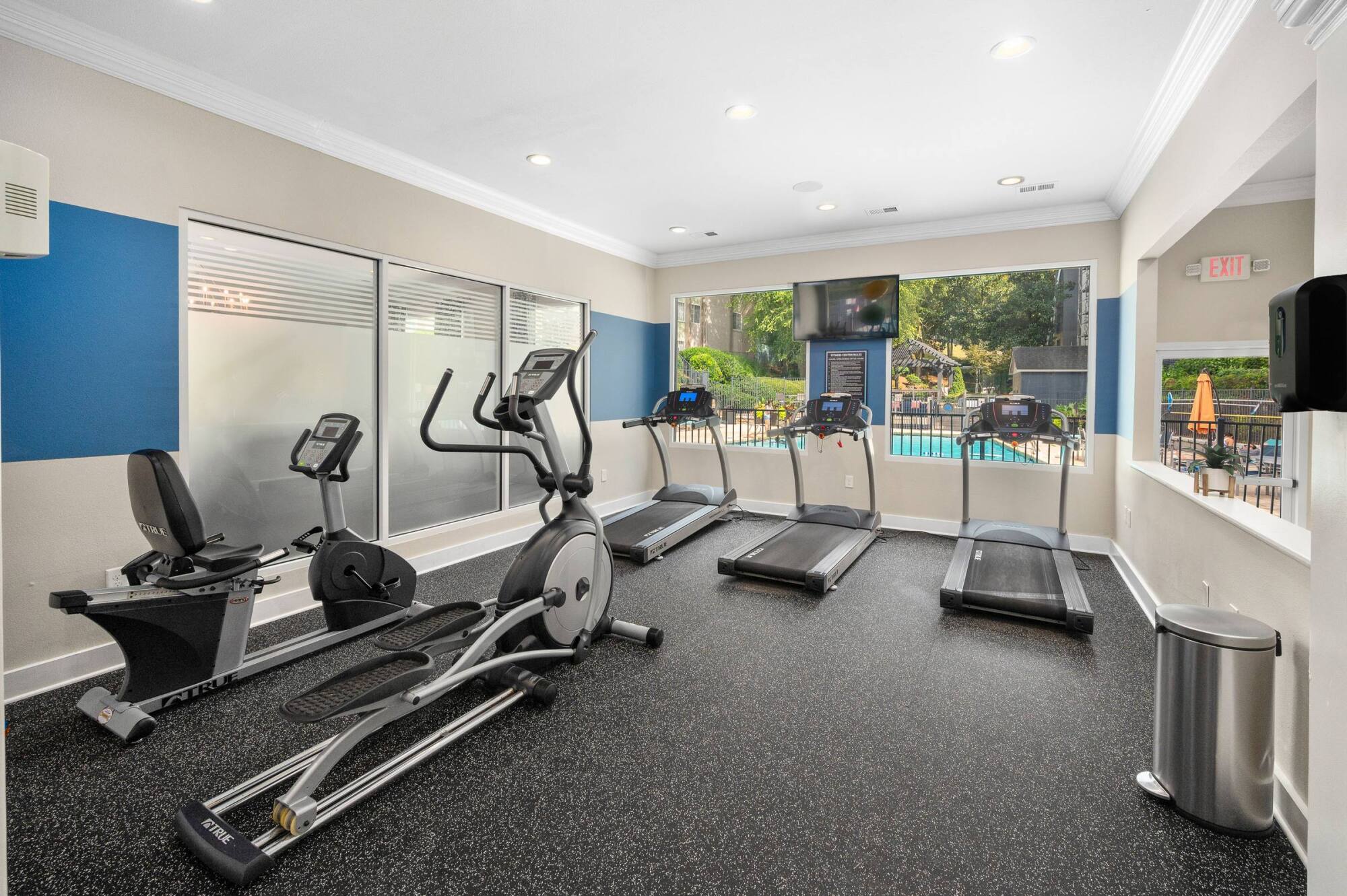 Cardio room at The Whitney with treadmills and an elliptical facing windows that overlook the swimming pool.