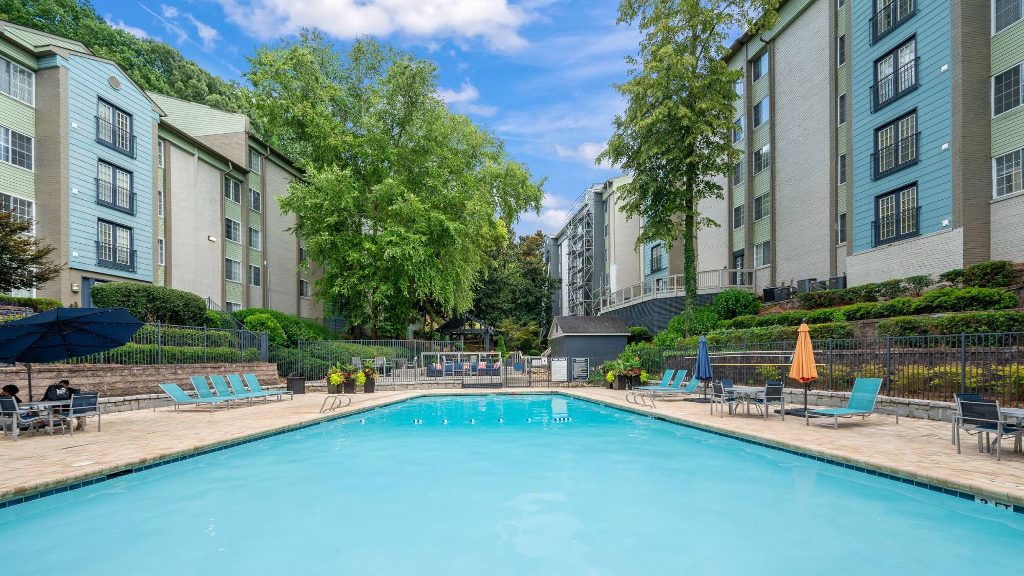 Swimming pool at The Whitney in Atlanta, GA surrounded by lounge chairs, umbrella tables, and leafy shade trees.