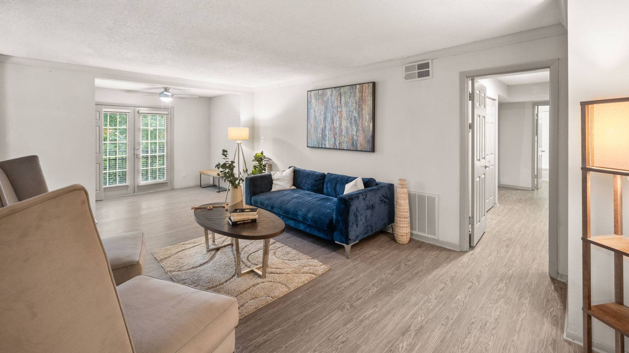Open living area at The Whitney with wood-plank vinyl flooring, a blue sofa, and a bright wall of patio doors.
