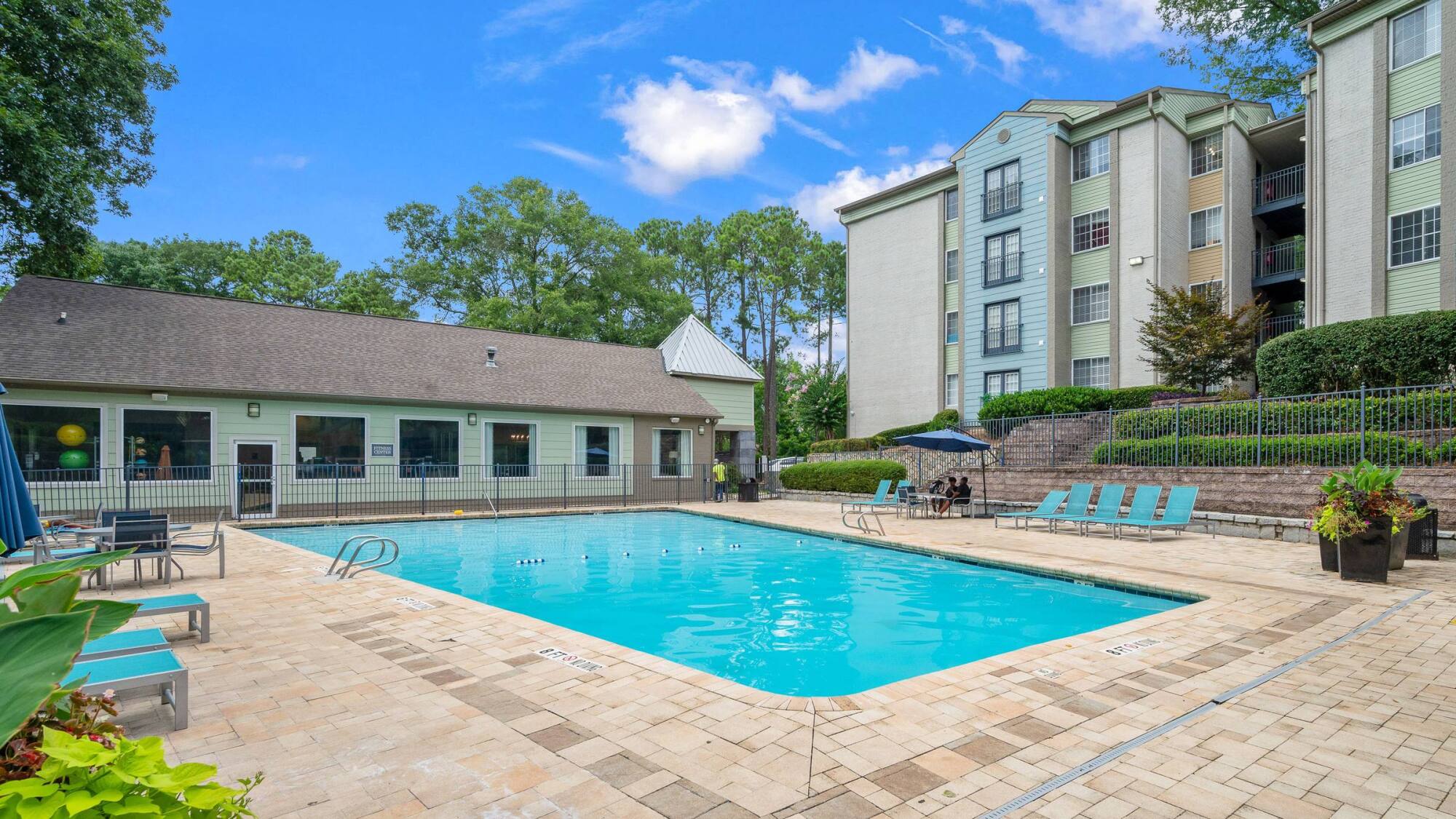 Outdoor pool at The Whitney in Atlanta, GA with a paver sundeck, lounge chairs, and the clubhouse beside apartment buildings.