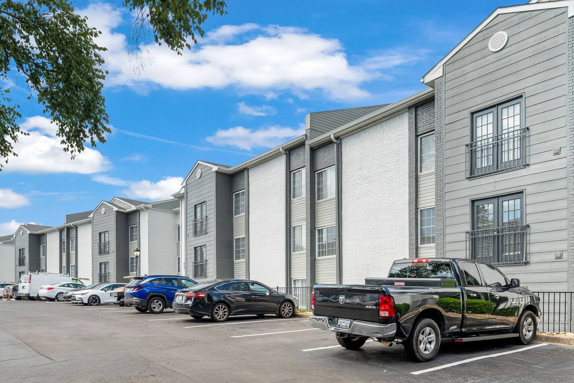 Grey and white brick apartment buildings at The Whitney in Atlanta, GA, with resident parking and mature shade trees.