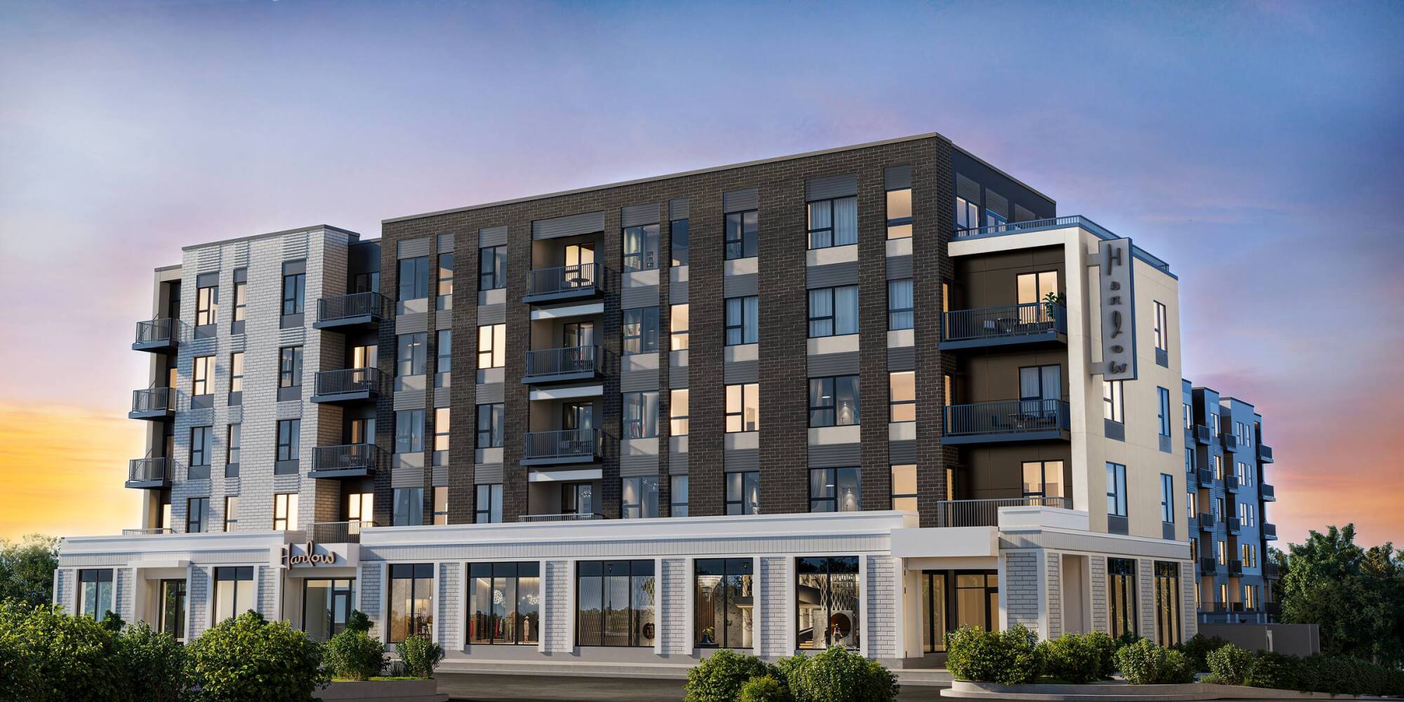 Modern five-story apartment building with balconies, large windows, and evening lighting against a sunset sky.