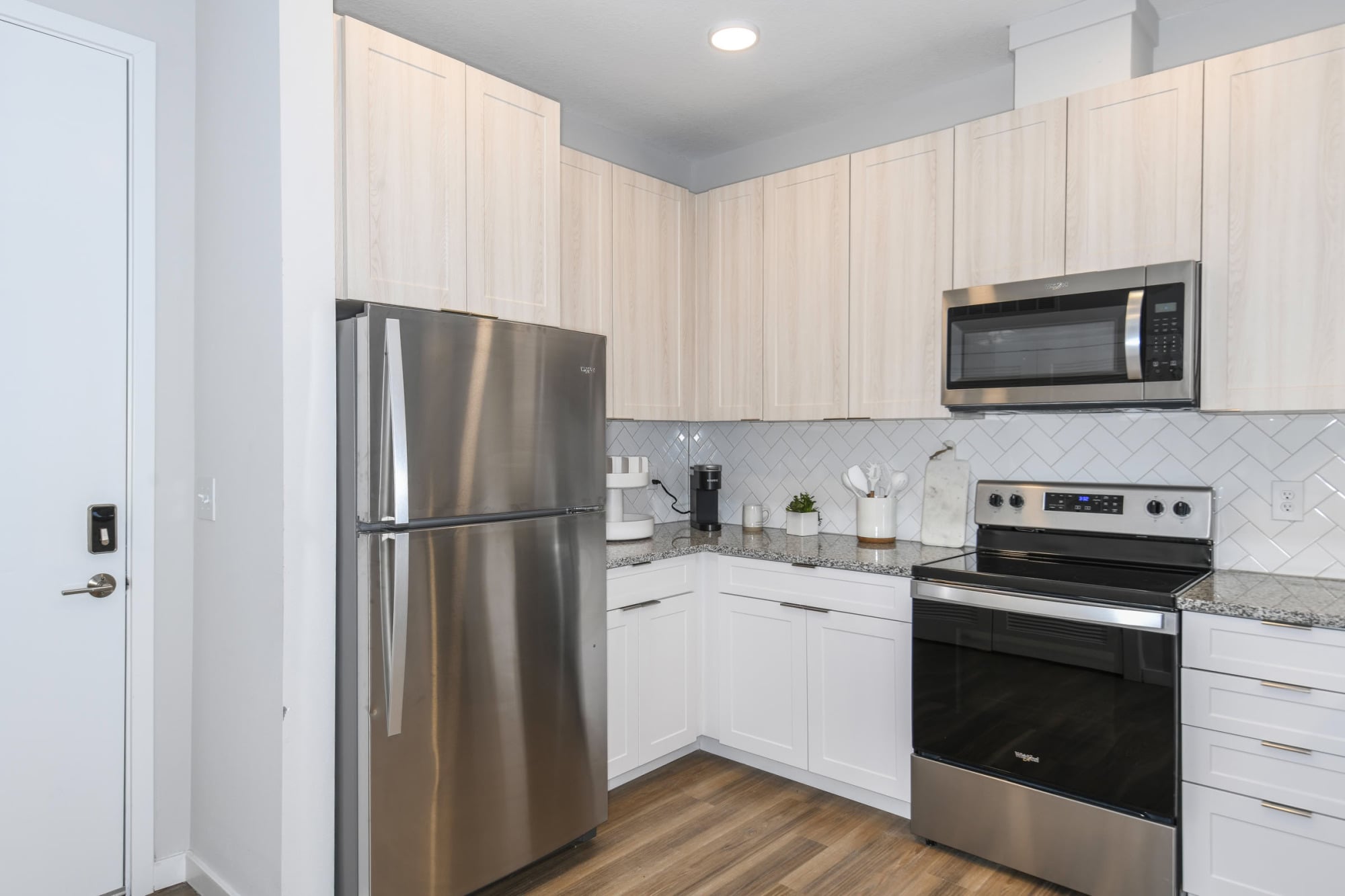 Apartment kitchen with stainless steel appliances, light wood cabinets, and herringbone tile backsplash at The Griffin