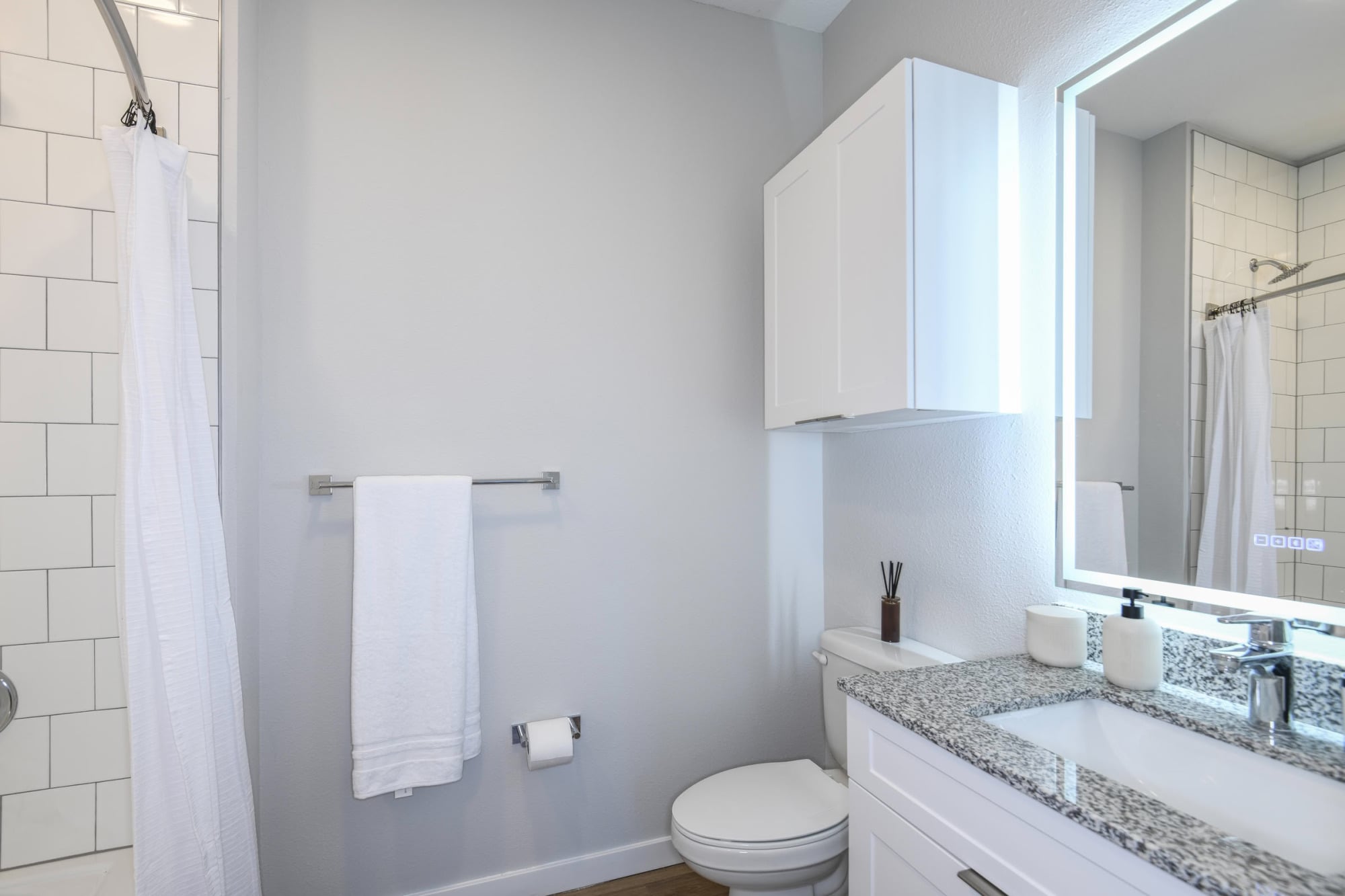 Apartment bathroom with backlit mirror, granite vanity, and subway-tiled tub-shower at The Griffin