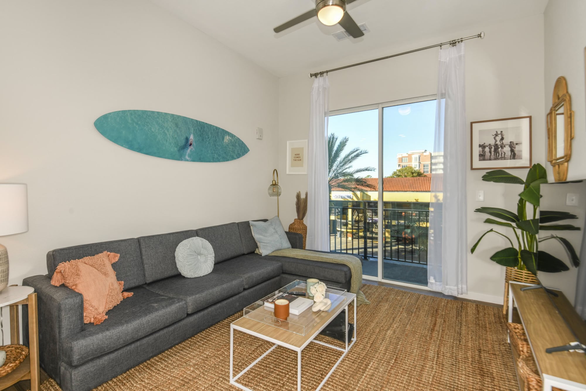 Apartment living room with gray sectional, surfboard wall art, and private balcony at Stadium House