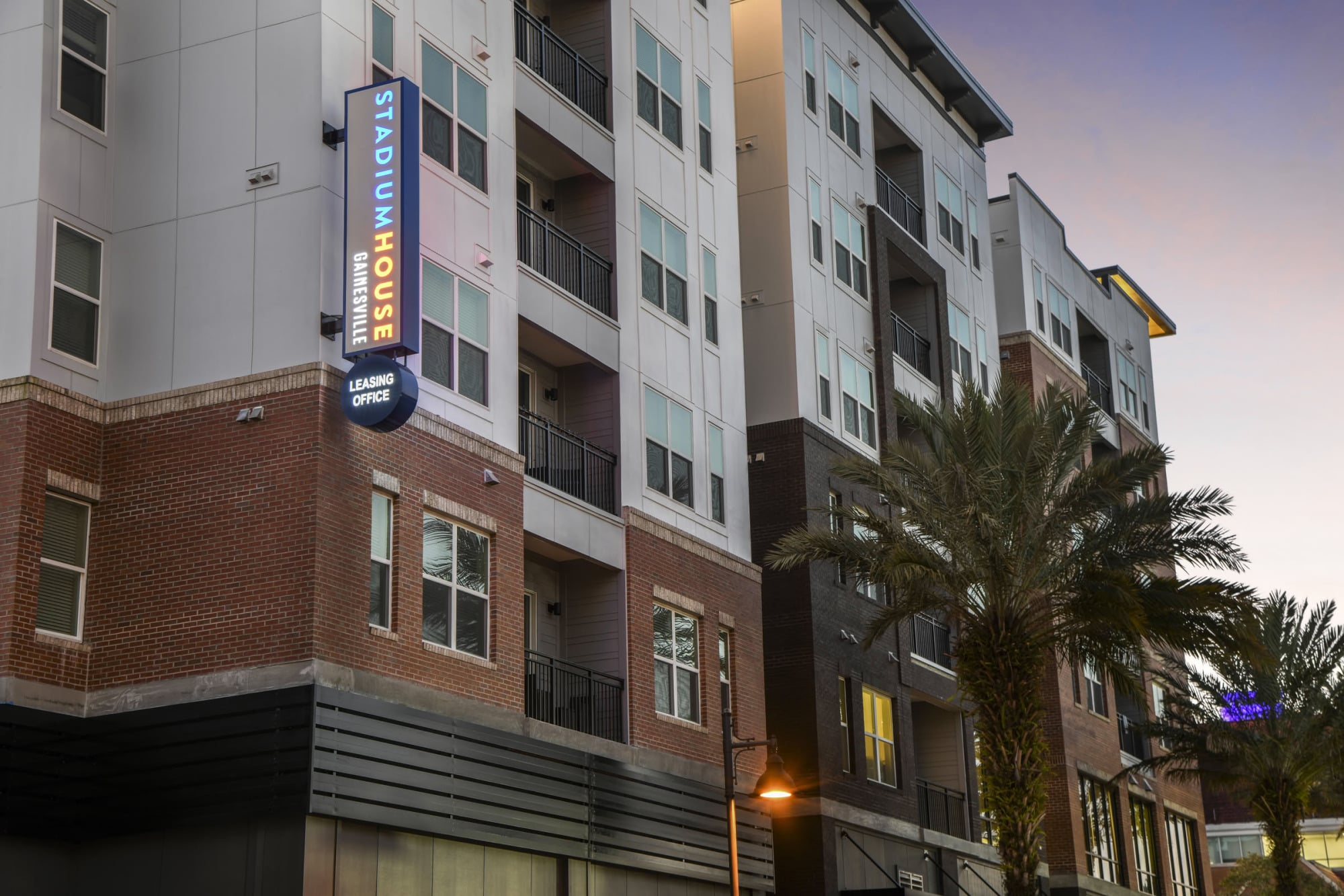 Close-up of Stadium House Gainesville leasing office sign on the brick apartment exterior at dusk