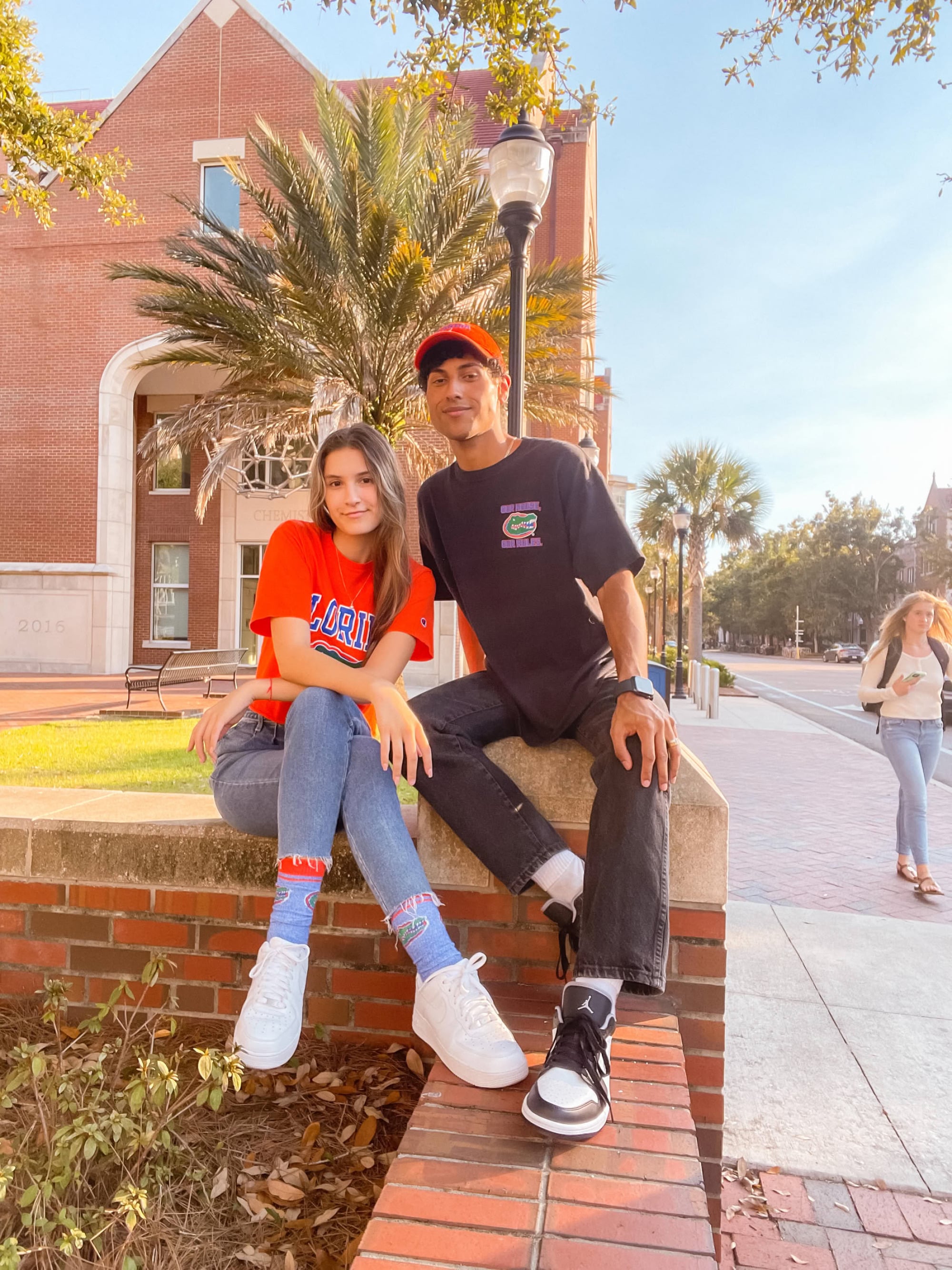 Young couple in Florida Gators gear posing on a brick ledge in front of a campus building