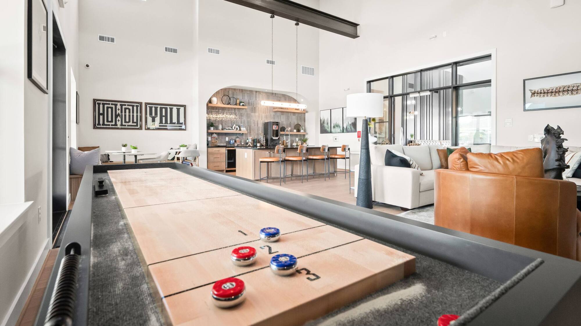Modern living space with a shuffleboard table, kitchen, dining area, and stylish seating in an open layout.