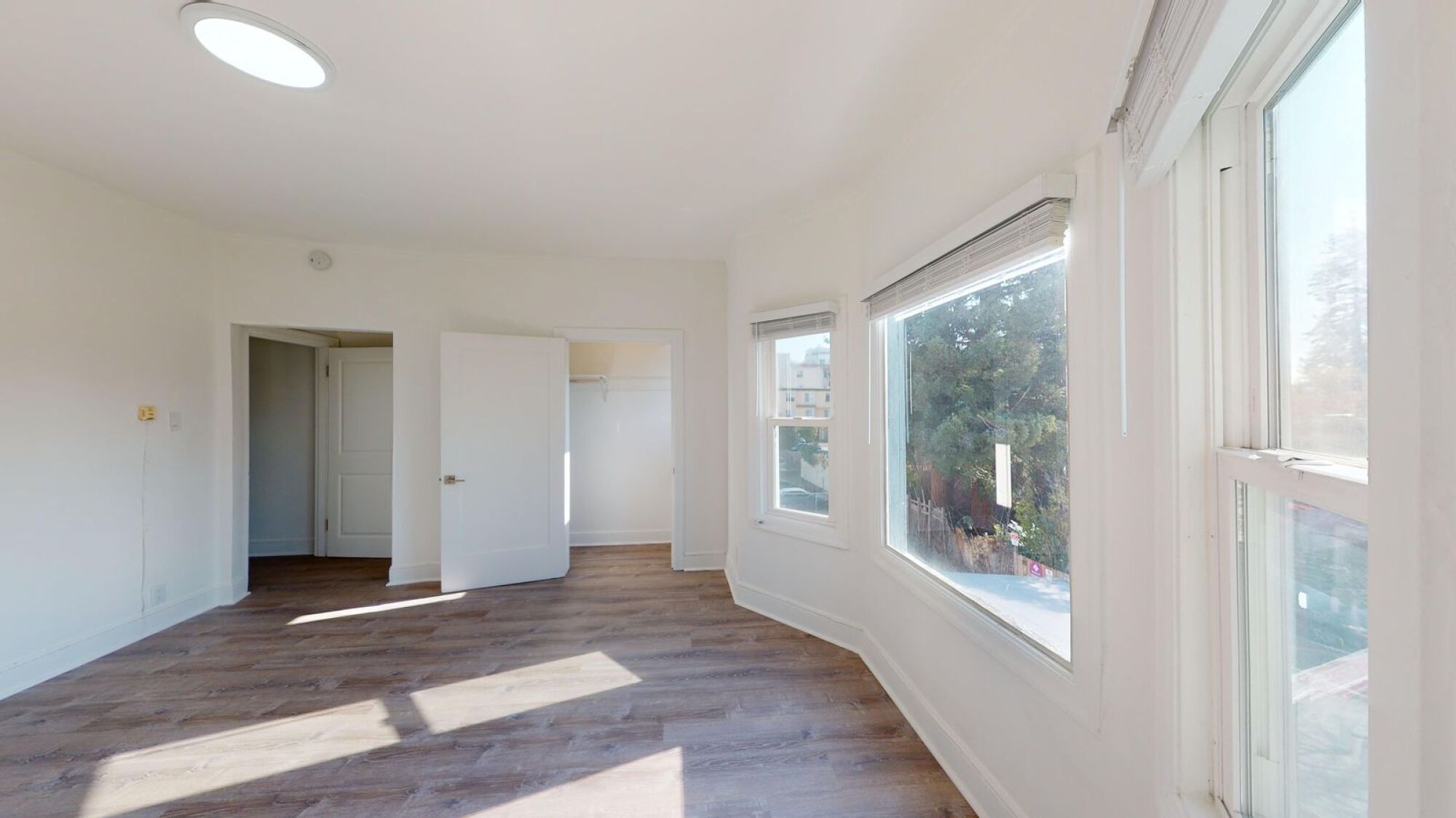 A room with white walls and wooden flooring with a window on the right side.