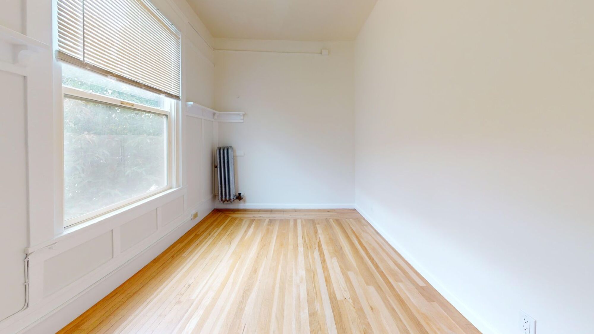 A room with wooden flooring and a window with blinds.