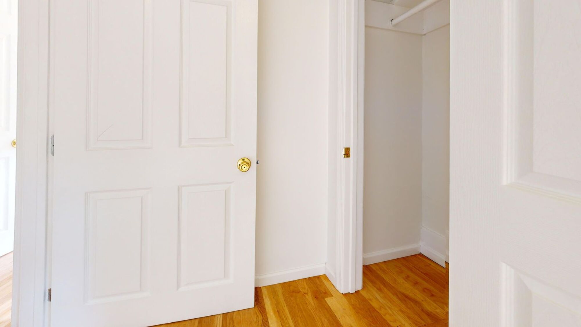 A white door with a gold handle is on the left and a white hallway is on the right.