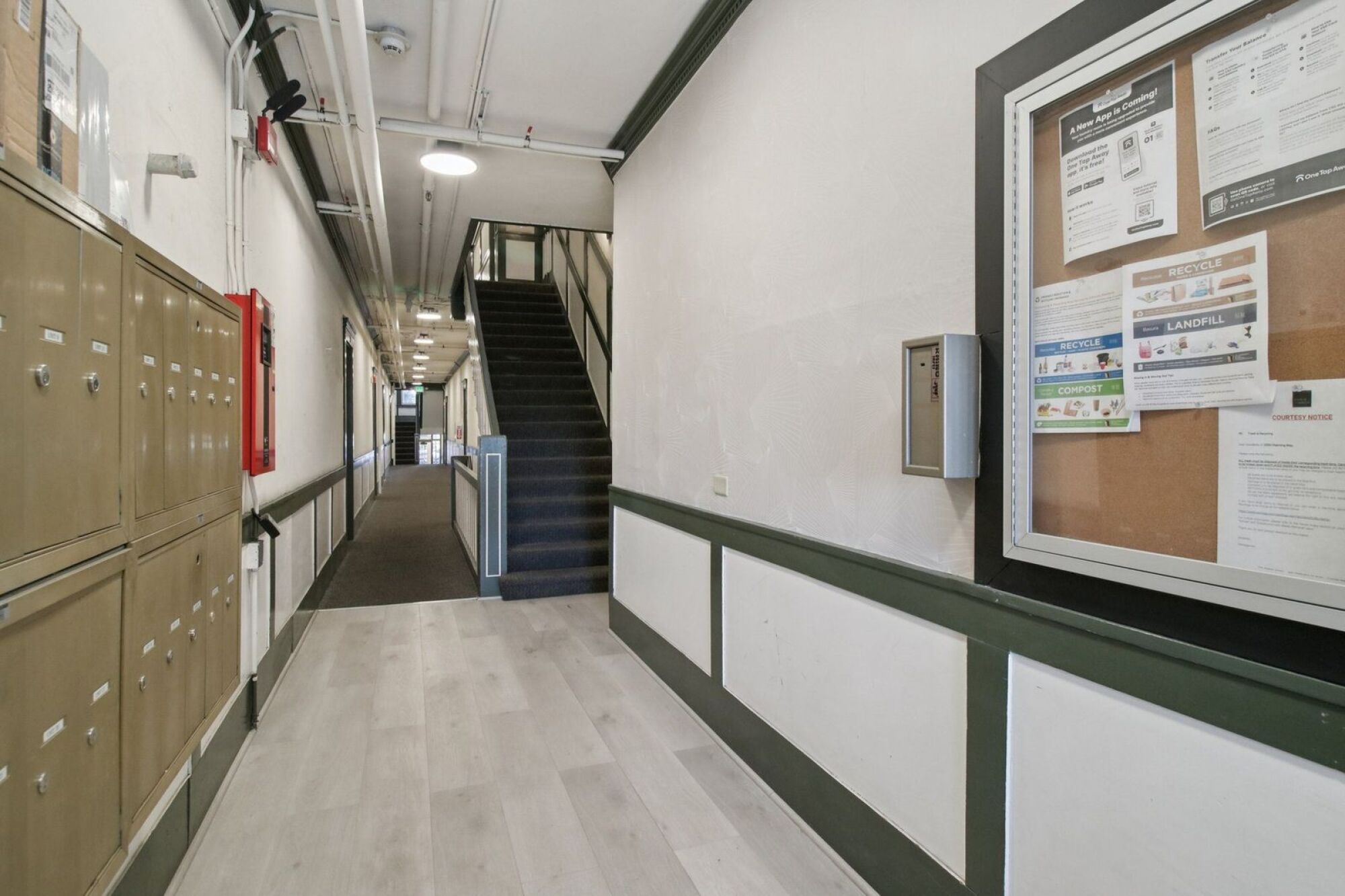 A long hallway with a bulletin board on the wall.