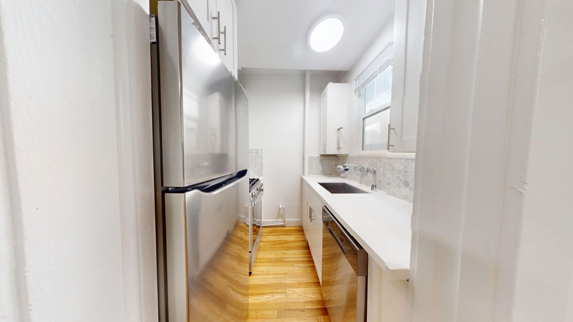 A small kitchen with a refrigerator, sink, and wooden floor.