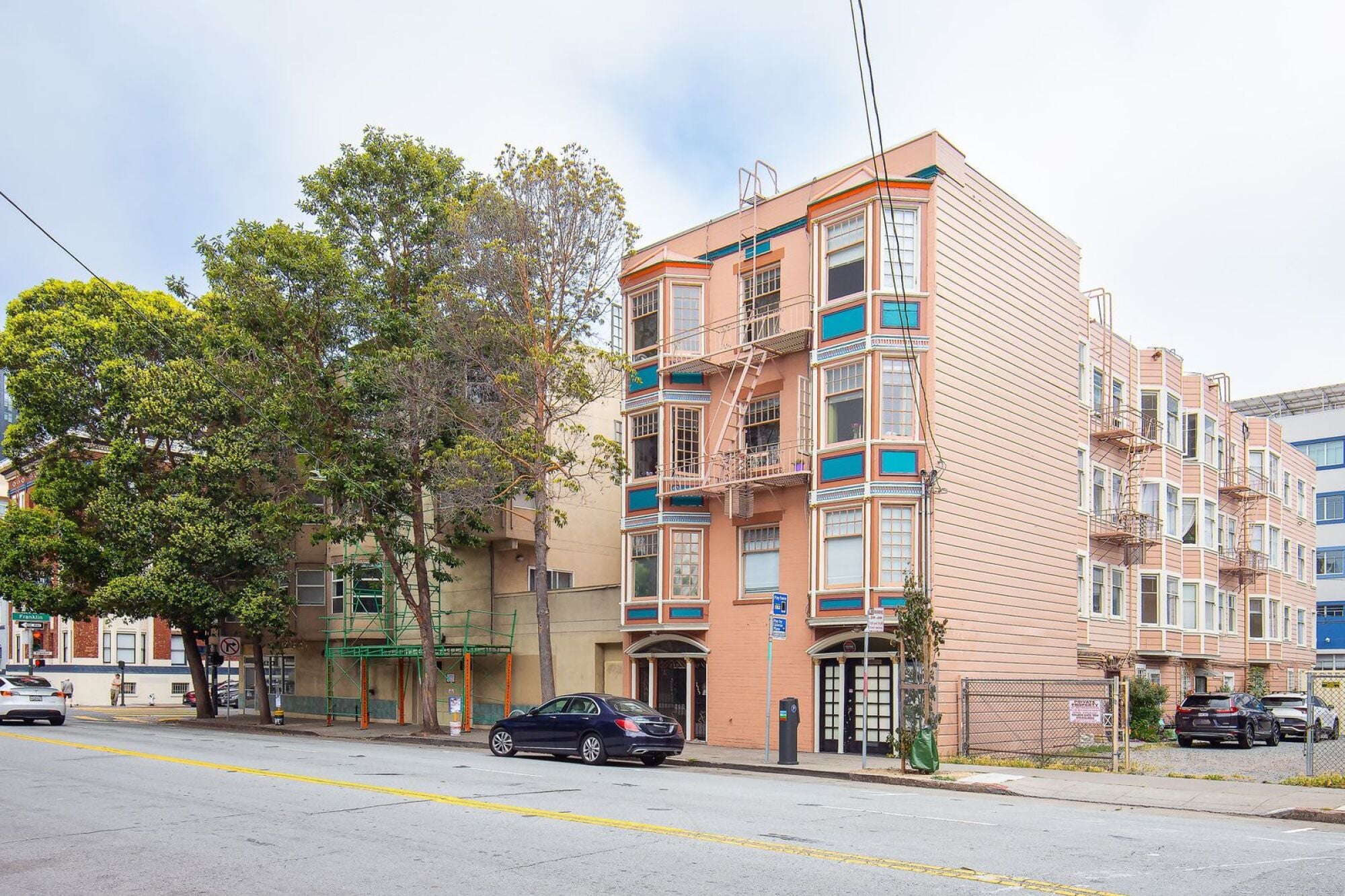 A street view of a multi-story building with cars parked in front.