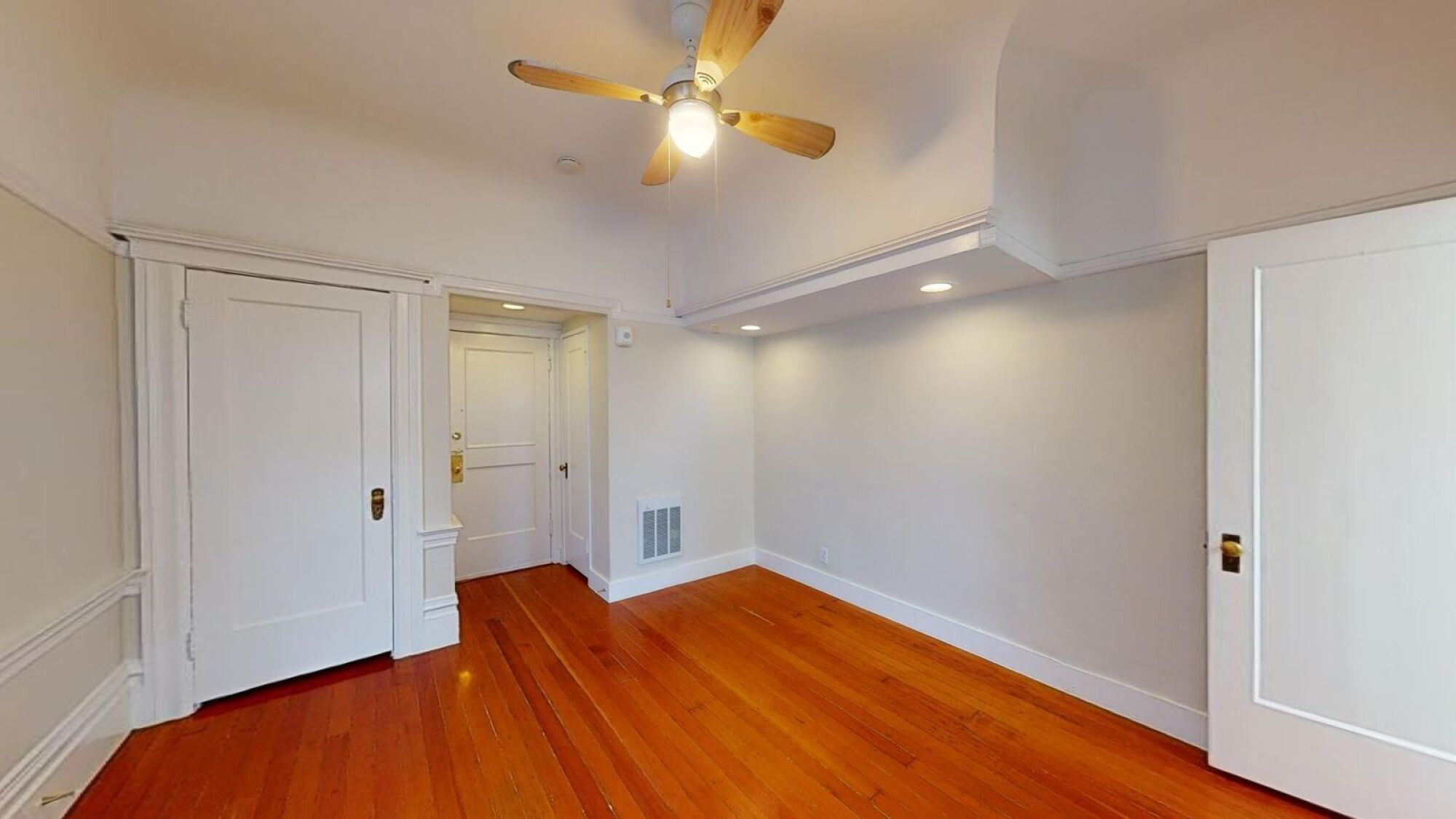 A room with a ceiling fan and wooden floors.
