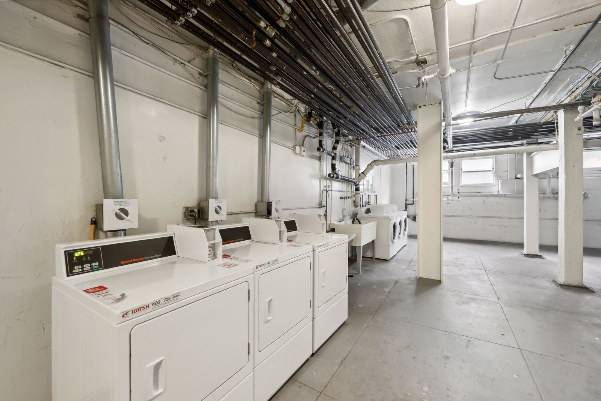 A row of industrial washing machines are lined up in a clean, empty room.