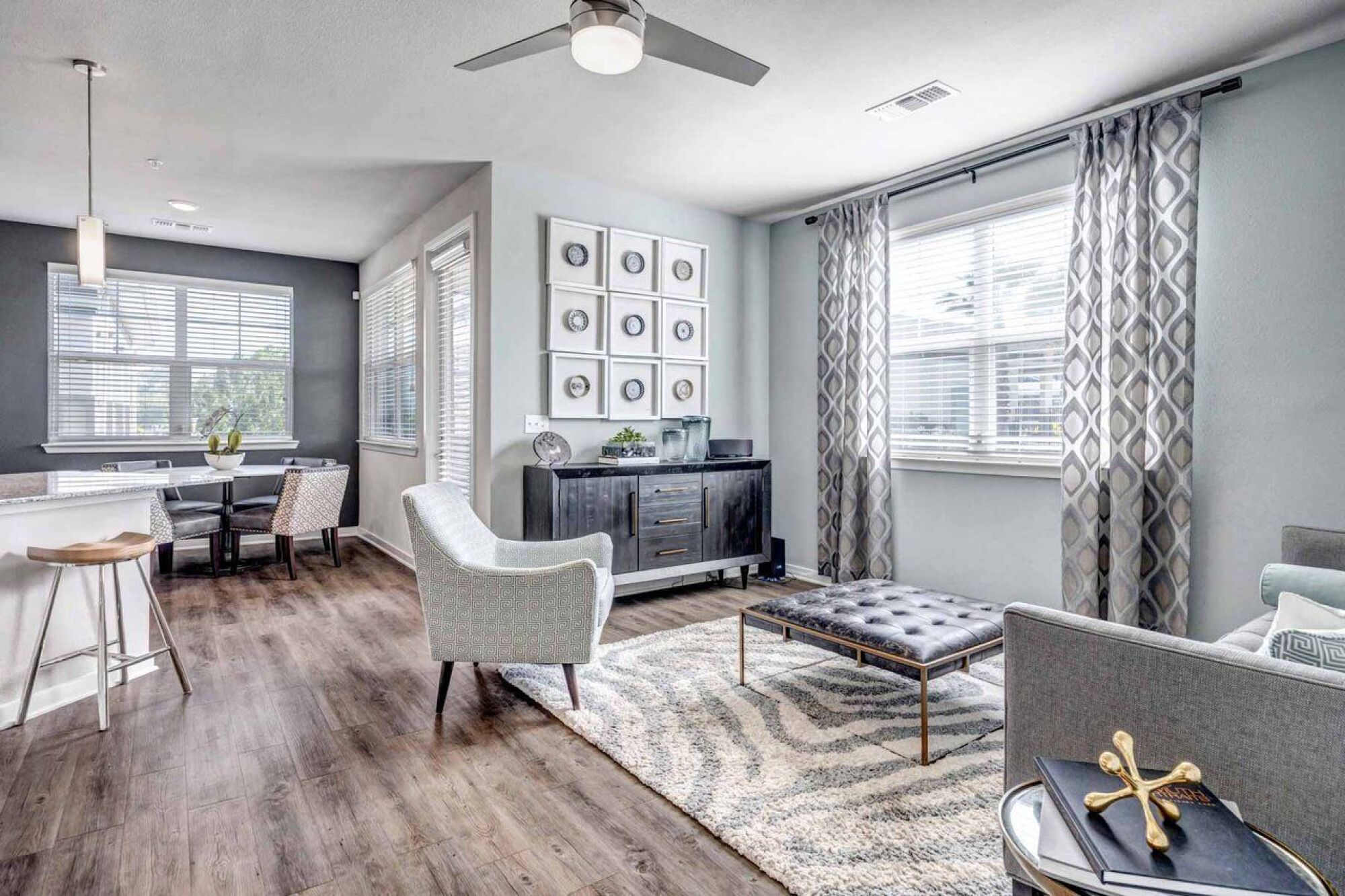 Modern living room with gray furniture, patterned rug, wall art, and large windows letting in natural light at Luminary at 95 apartments.