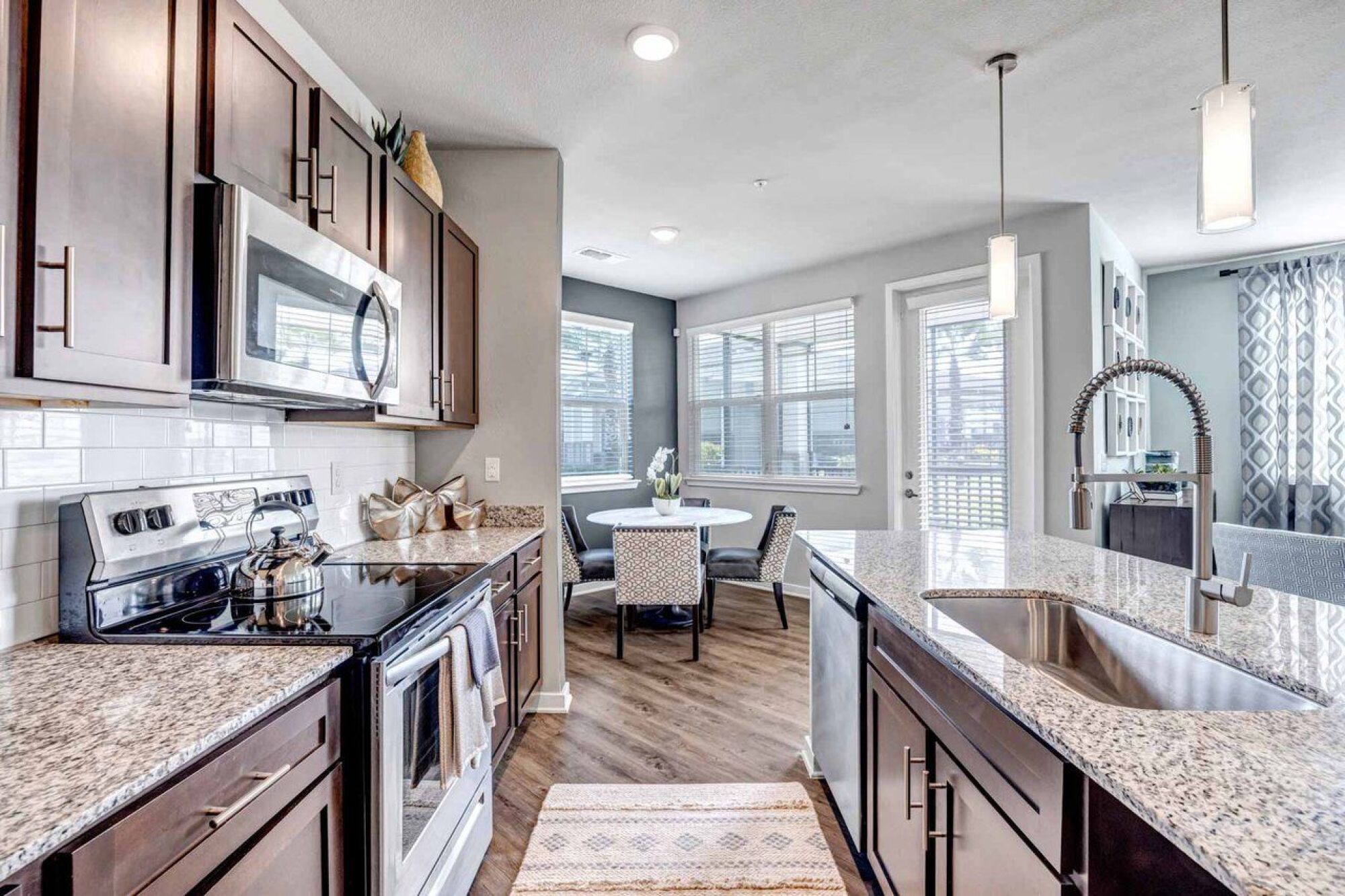 Modern kitchen with stainless steel appliances, granite countertops, and a dining area by large windows at Luminary at 95 apartments.