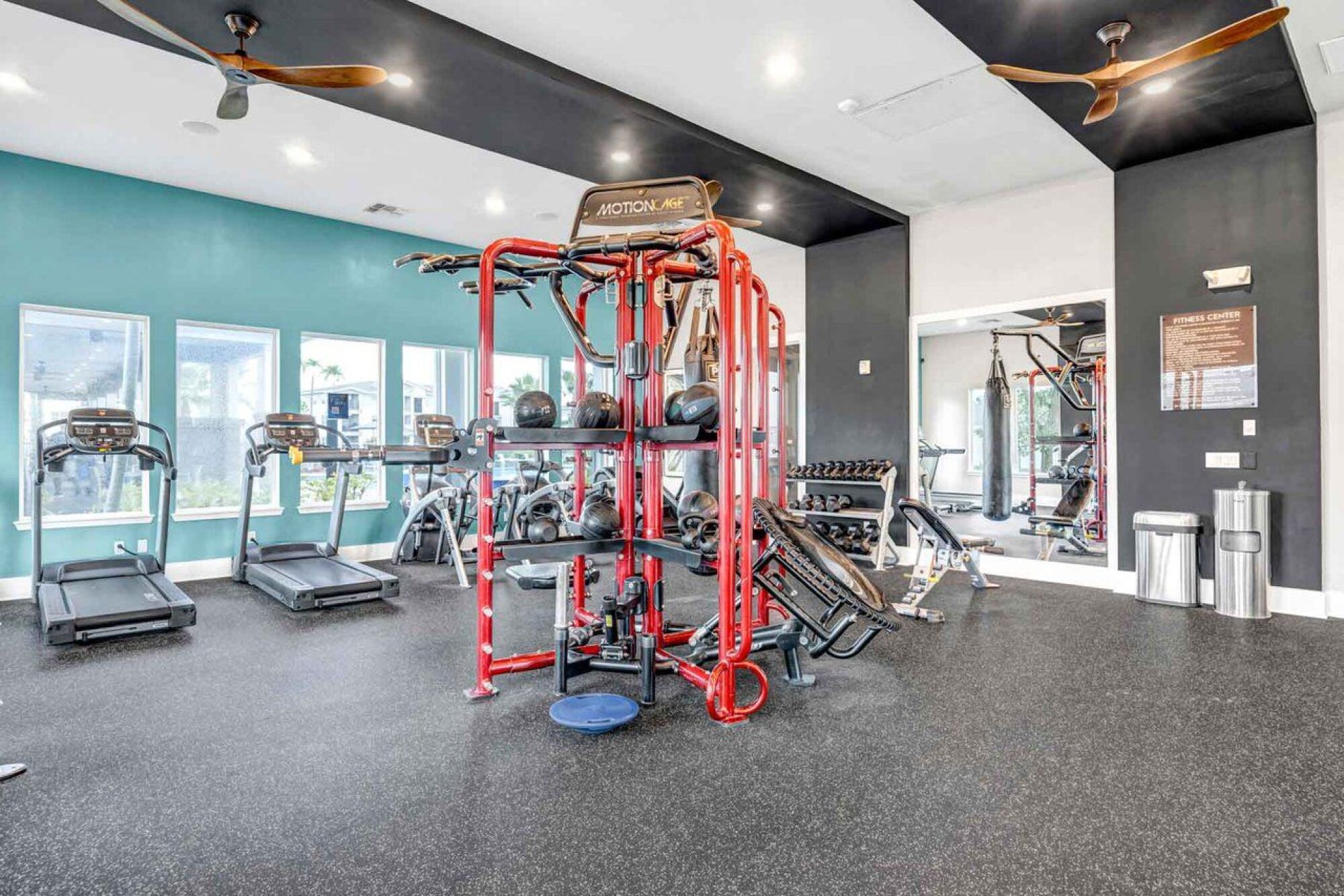 Modern gym with various exercise machines, free weights, and a red multi-station workout unit in the center at Luminary at 95 apartments.