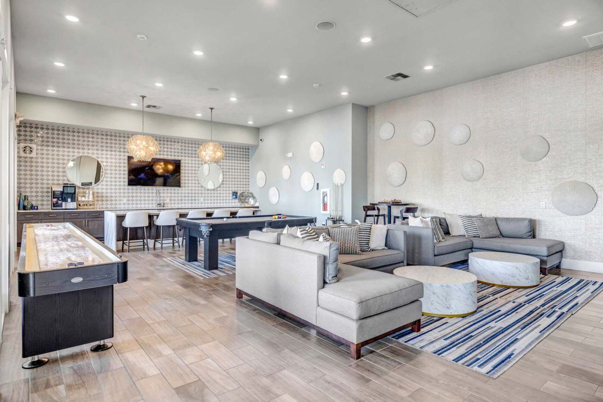 Modern lounge with gray sofas, pool table, bar seating, patterned wall, and round decorative wall art at Luminary at 95.