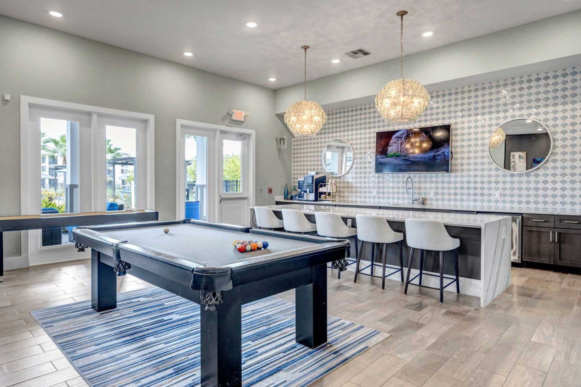 Modern game room with a pool table, bar seating, TV, and stylish pendant lights above the counter at Luminary at 95 apartments.