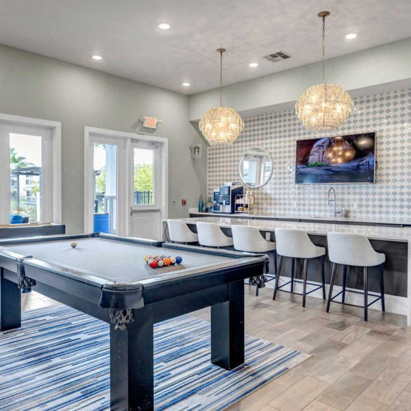 Modern game room with a pool table, bar seating, TV, and stylish pendant lights above the counter at Luminary at 95 apartments.