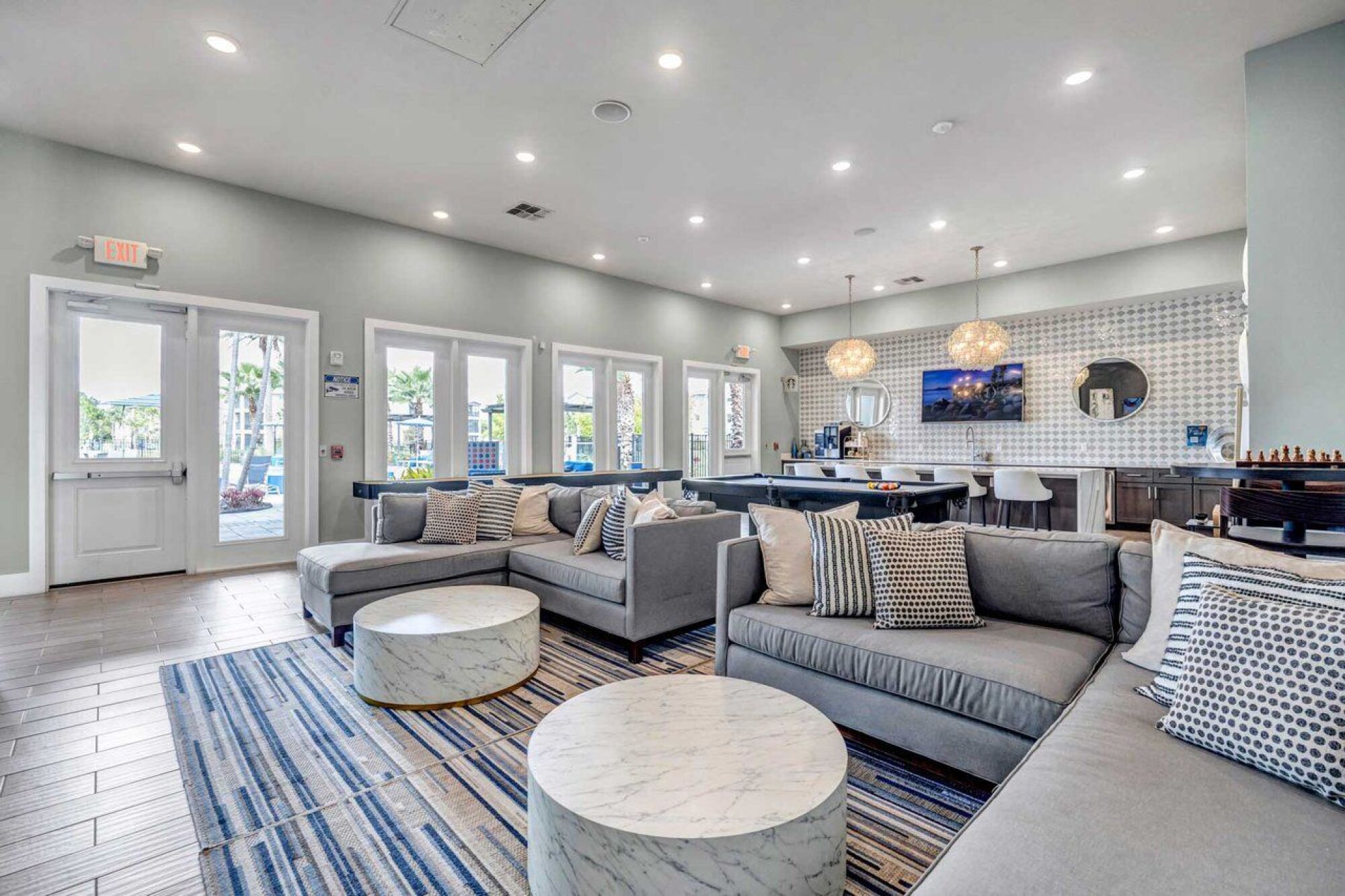 Modern lounge with gray sofas, marble tables, striped rug, and bar area with stools and pendant lights at Luminary at 95 apartments.