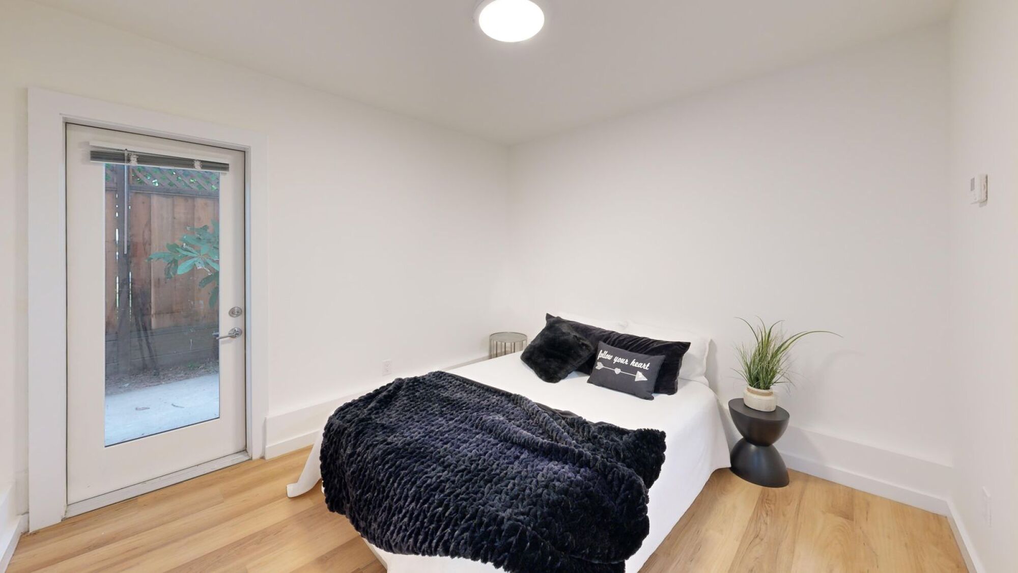 A bedroom with a bed, pillows, and a plant.