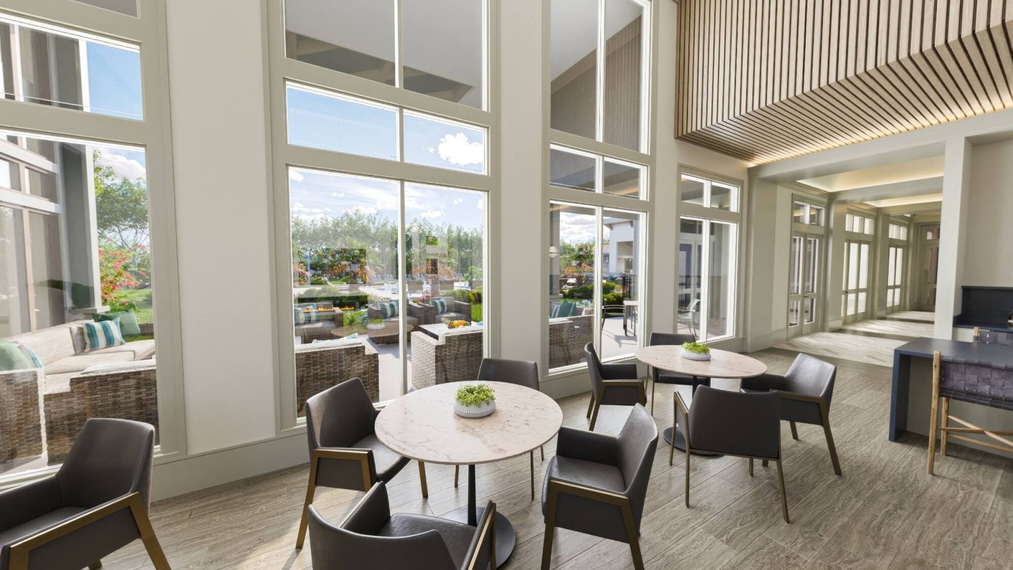 Modern lounge with round tables, chairs, large windows, and outdoor patio seating visible in the background.