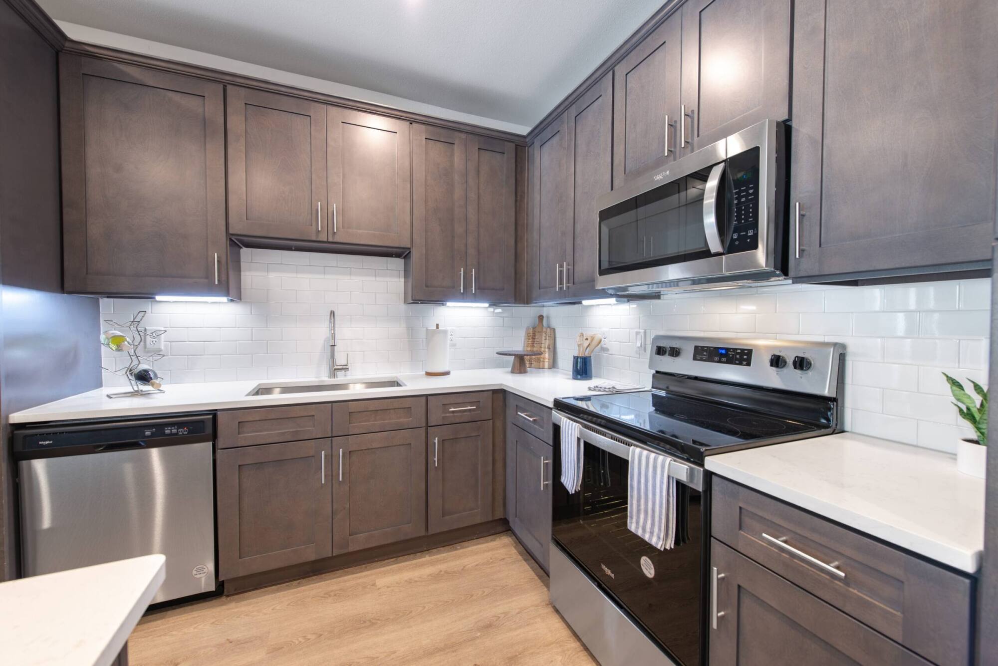 Modern kitchen with brown cabinets, stainless steel appliances, white countertops, and subway tile backsplash.