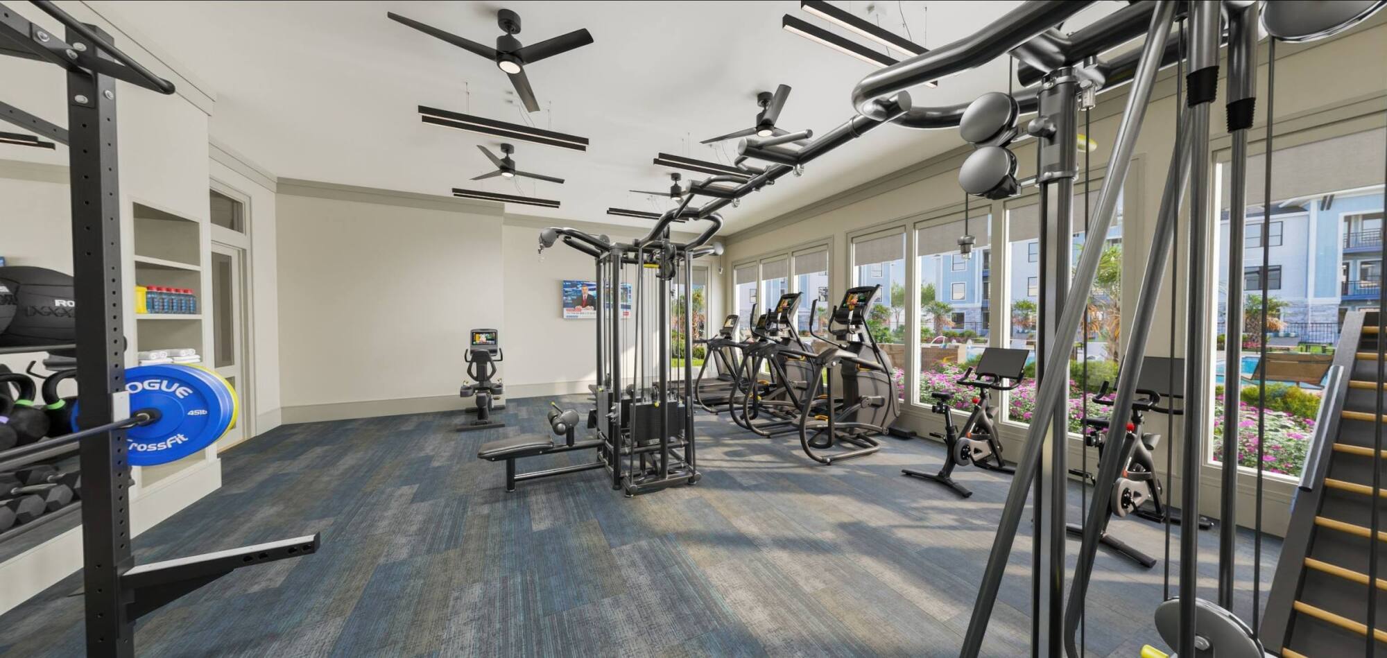 Modern gym with weight machines, cardio equipment, large windows, and plenty of natural light.