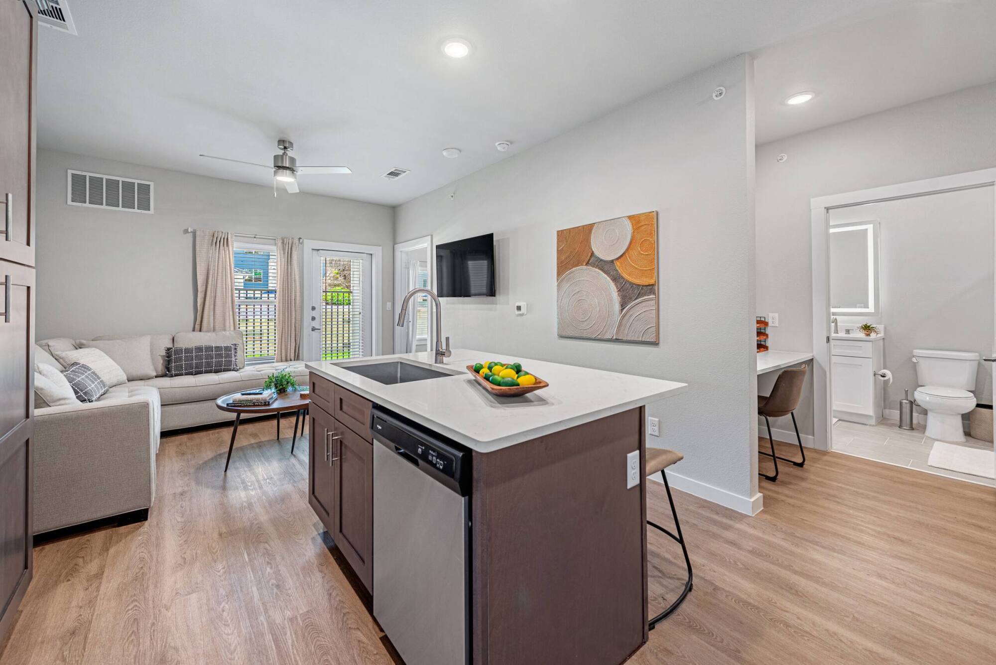 Modern open-concept kitchen and living area with island, sofa, wall art, and view into a bathroom.
