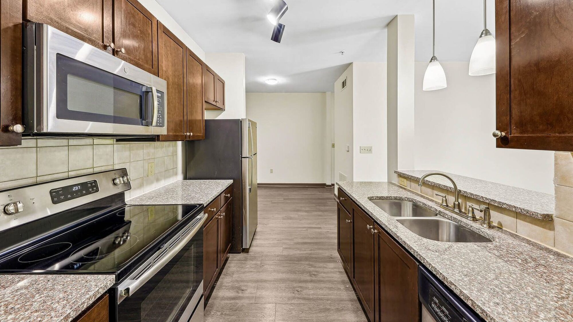 Modern kitchen with stainless steel appliances, wood cabinets, and granite countertops, viewed from the entrance at Apex West Midtown.