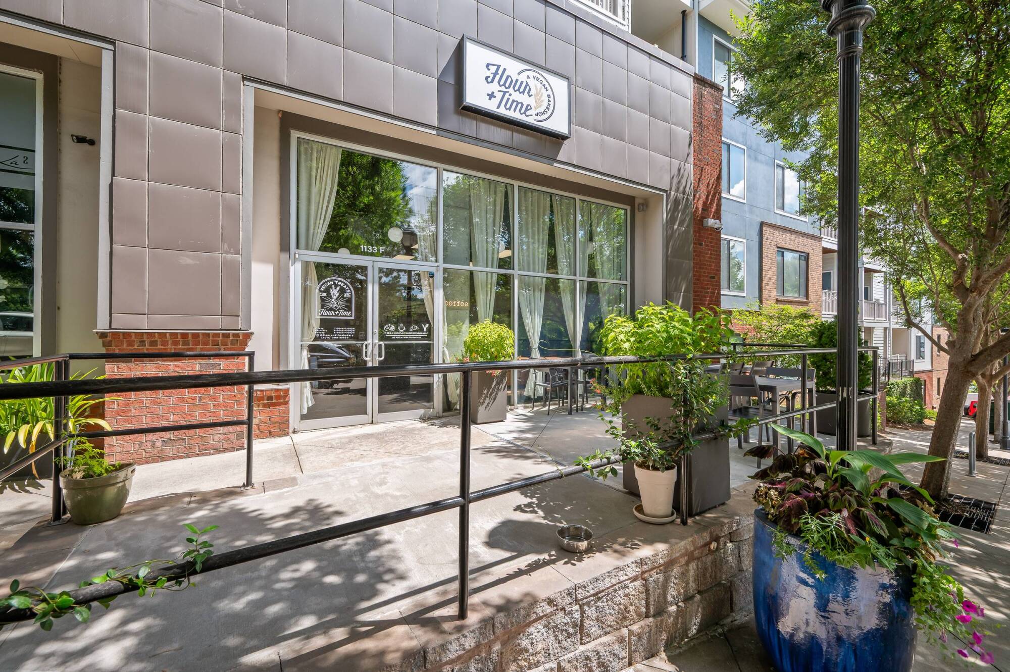 Entrance of a bakery café with large windows, potted plants, and a sign reading "Flour + Time.