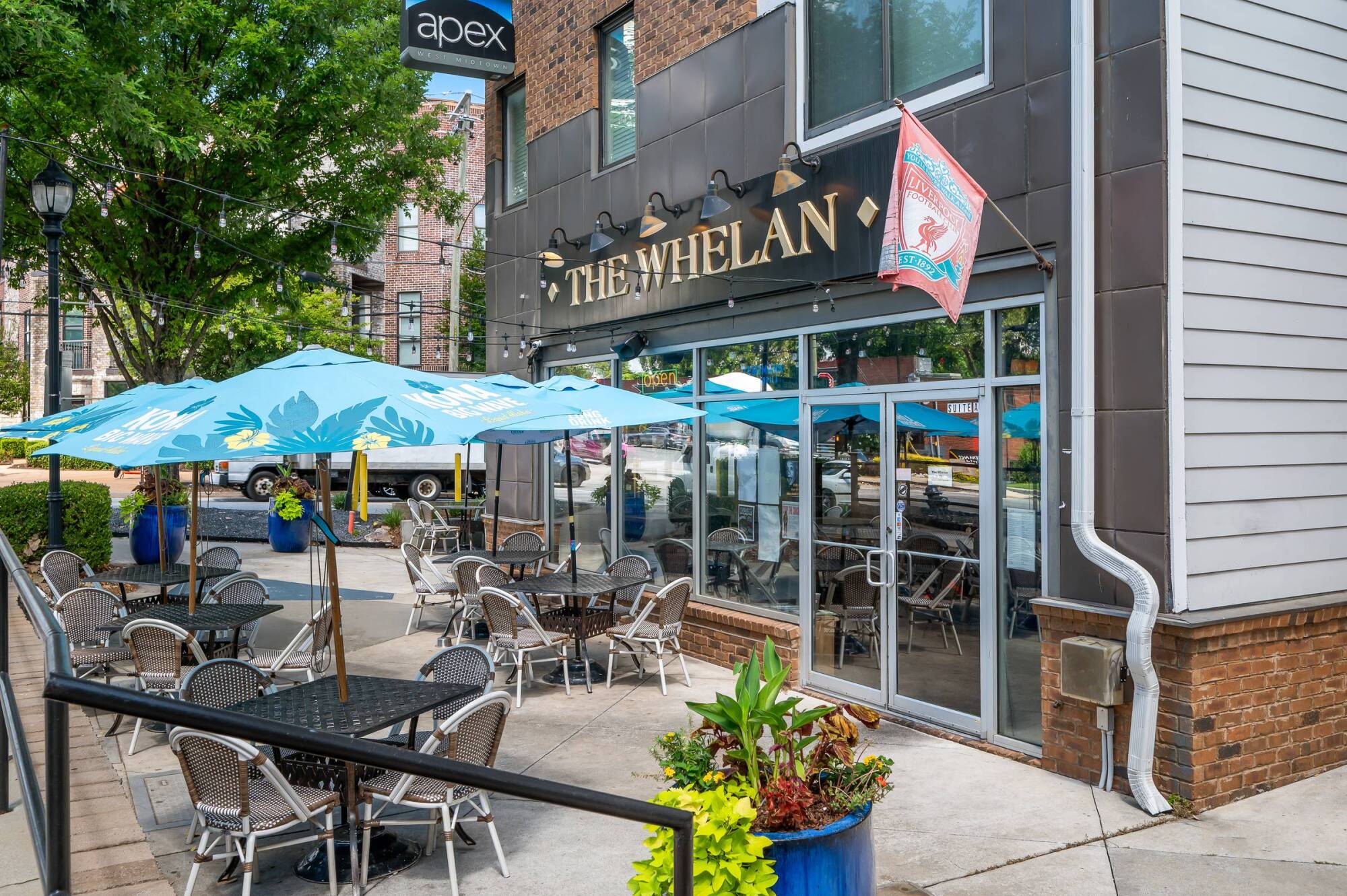 Outdoor patio seating with blue umbrellas in front of The Whelan restaurant on a sunny day.