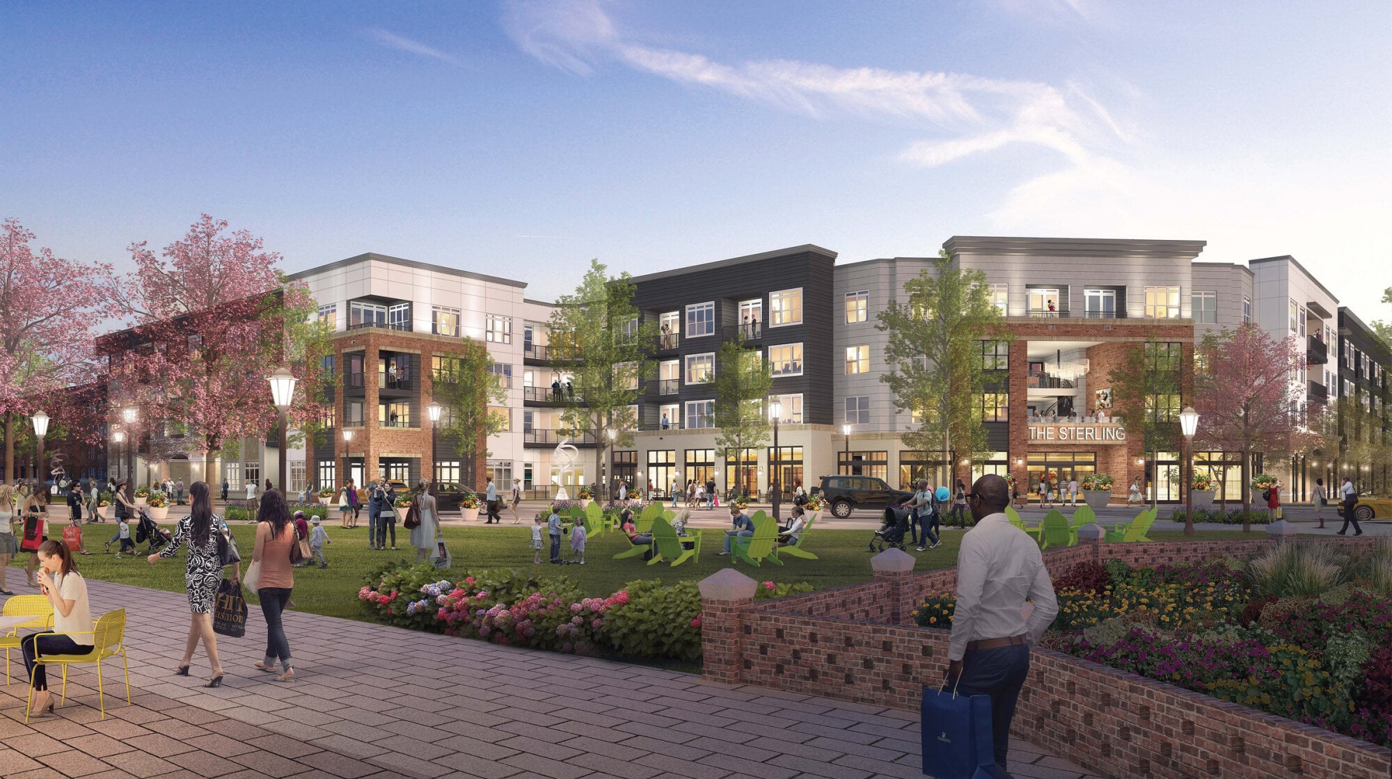 Residents relaxing on the landscaped lawn outside The Sterling's storefronts at dusk.