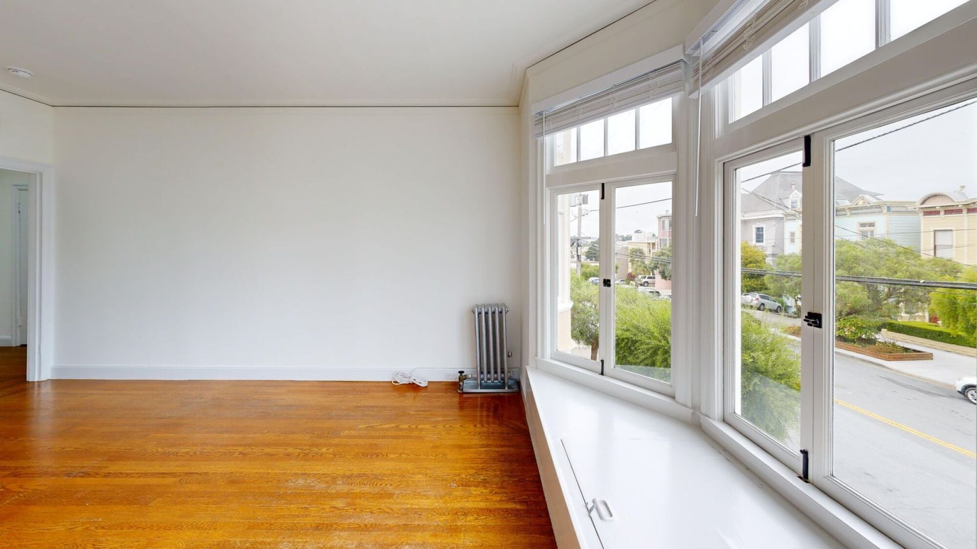 A room with a white wall and a window overlooking a street.
