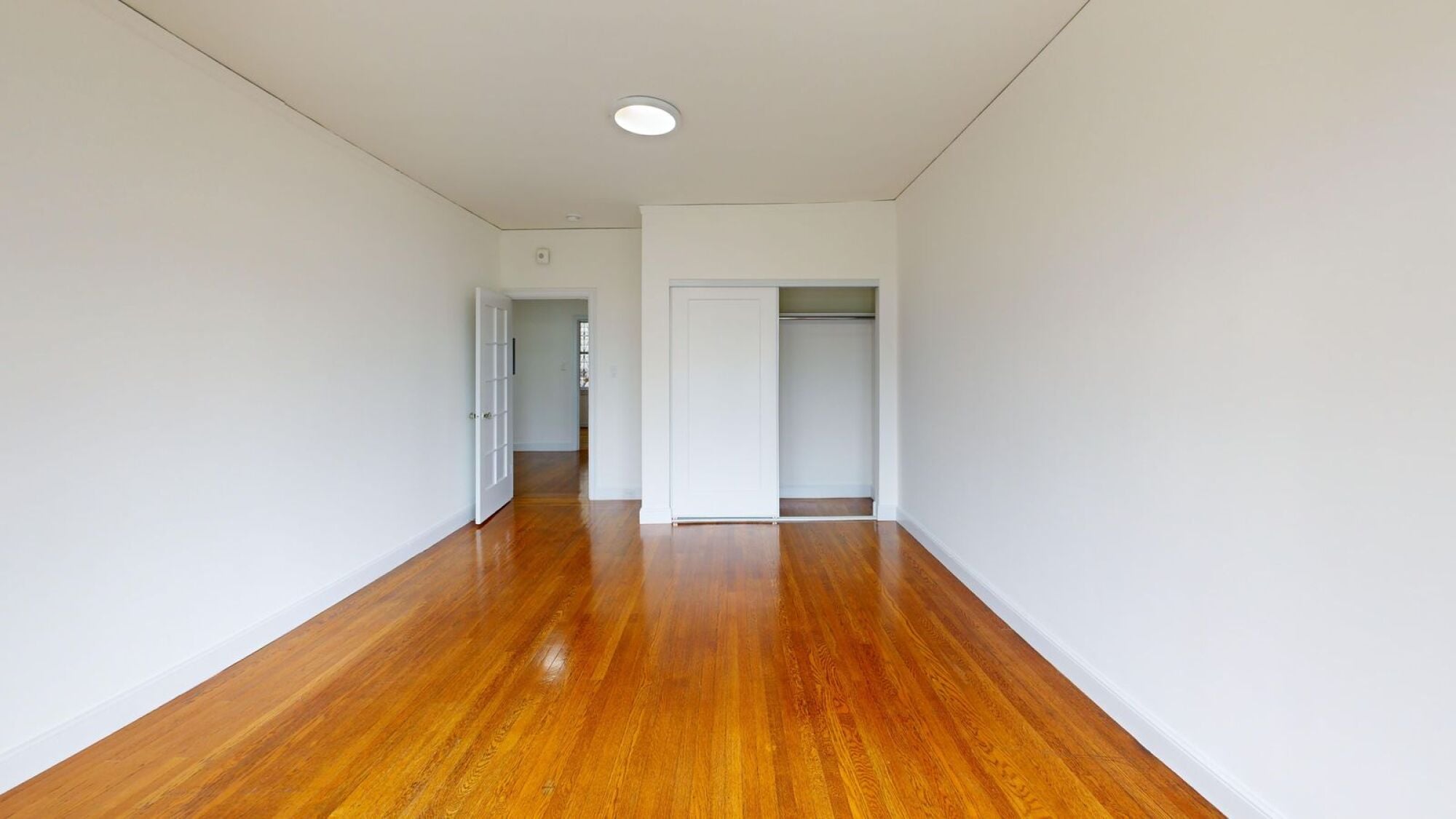 A long empty room with wooden floors and white walls.