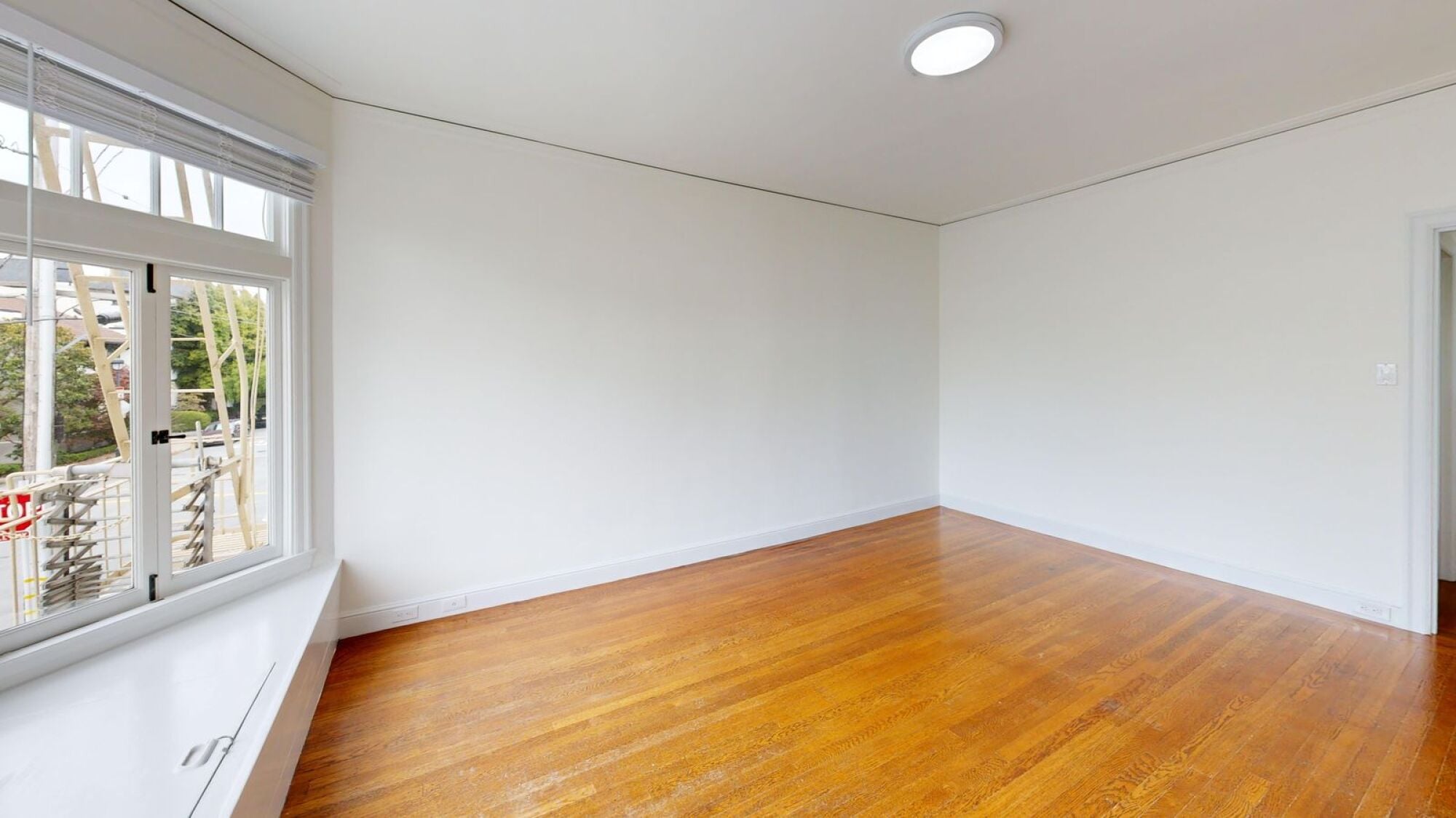 A room with wooden floors and a window overlooking a construction site.