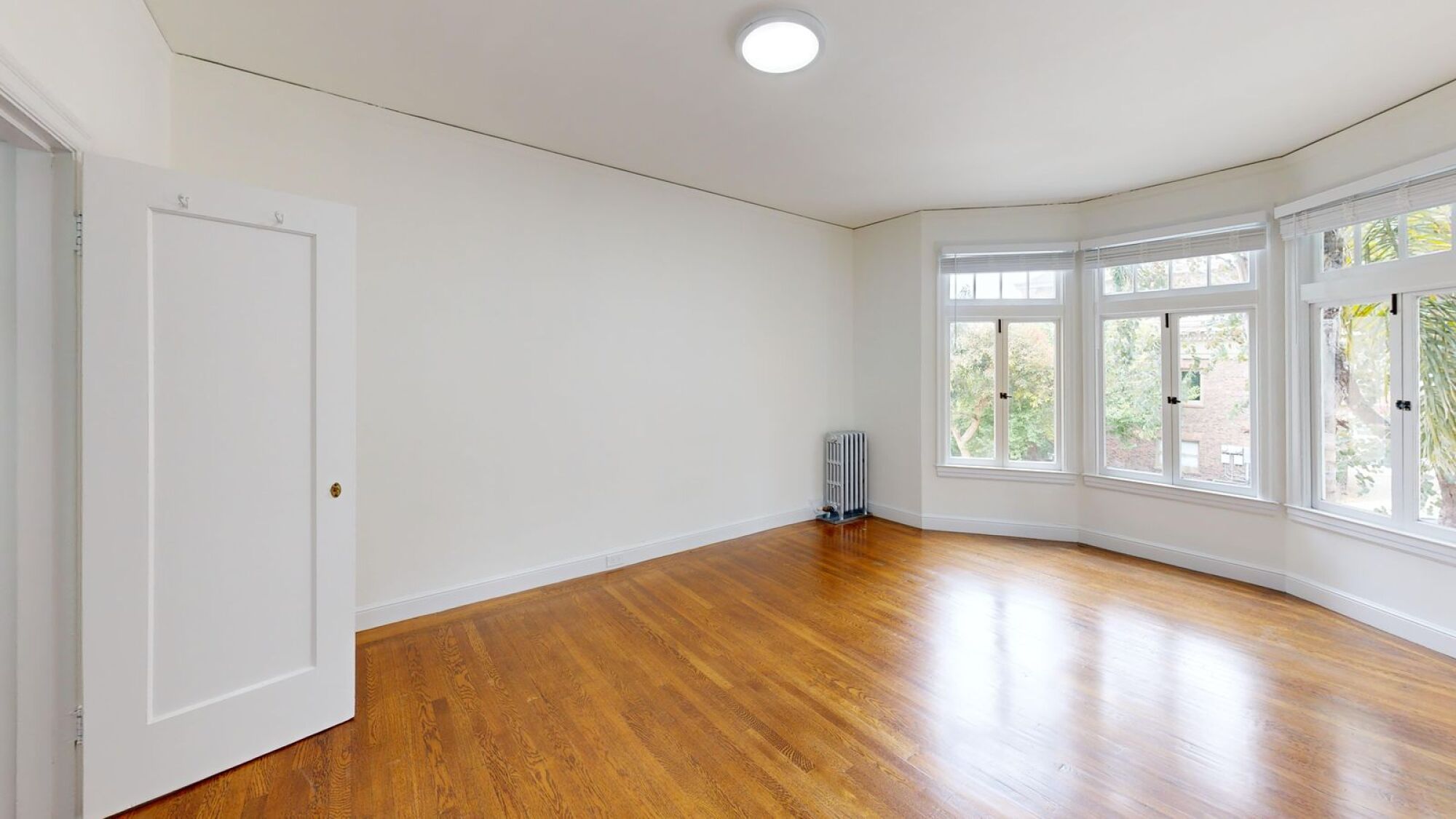 A room with a white door and a window with a view of trees.