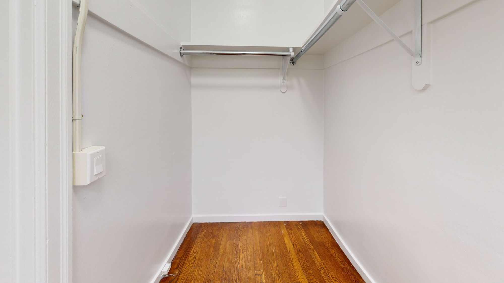 A white wall with a light switch and a white pipe.