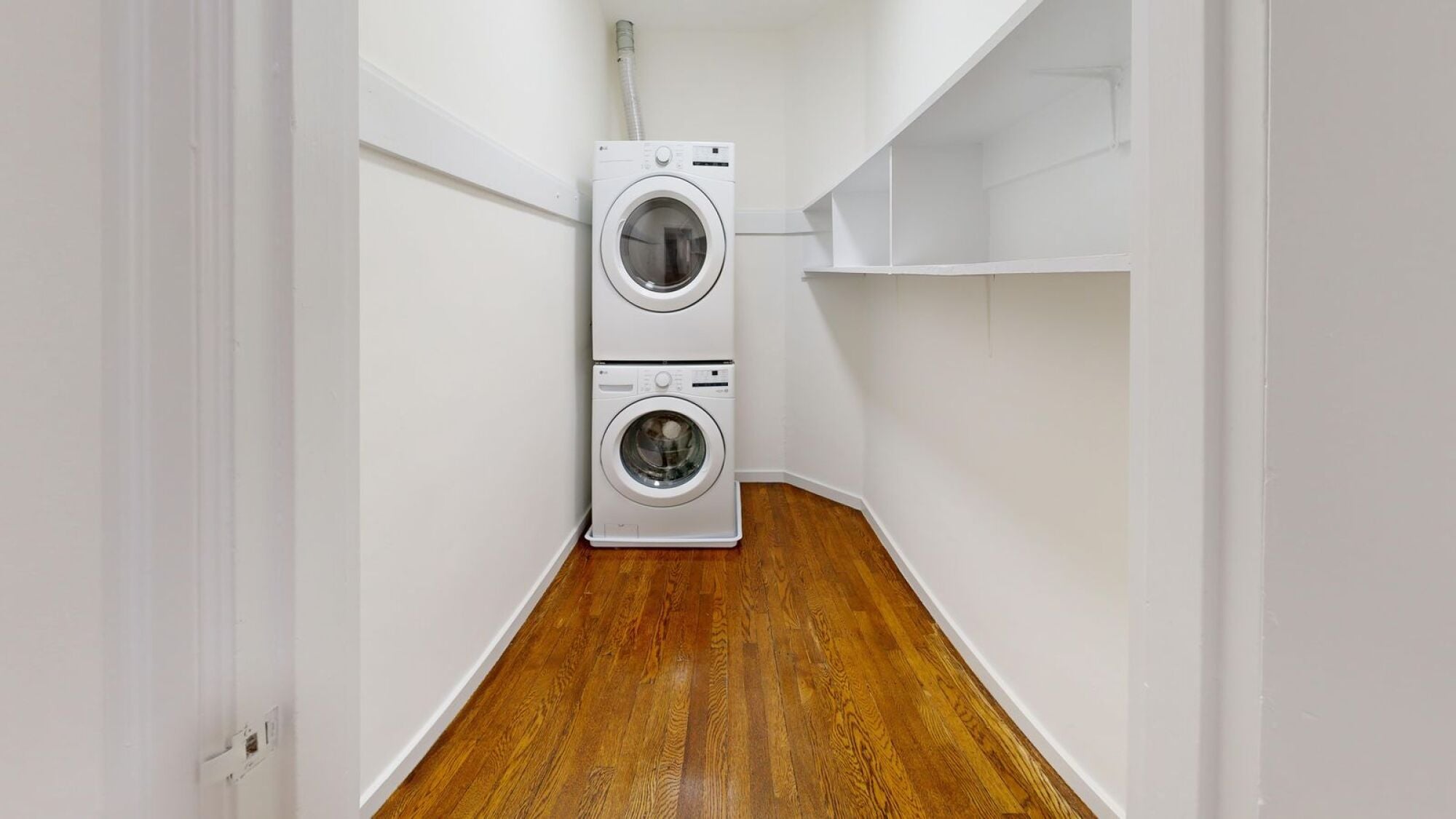 A white washing machine and dryer in a small room with wooden floors.