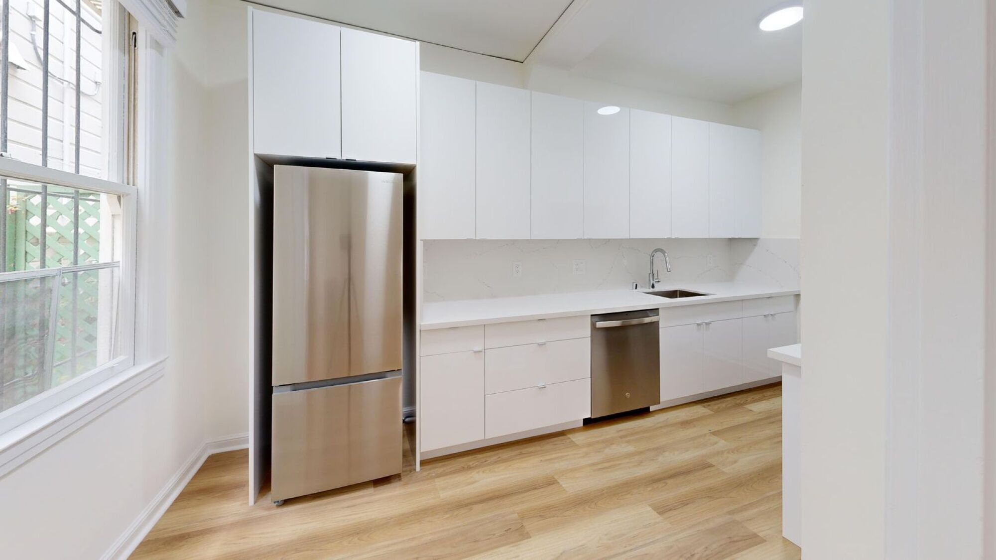 A modern kitchen with a stainless steel refrigerator and white cabinets.