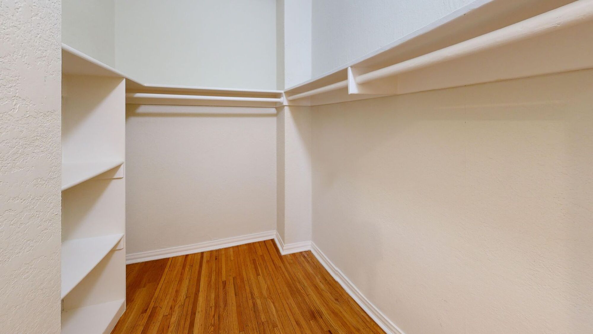 A white wall with a corner and a wooden floor.