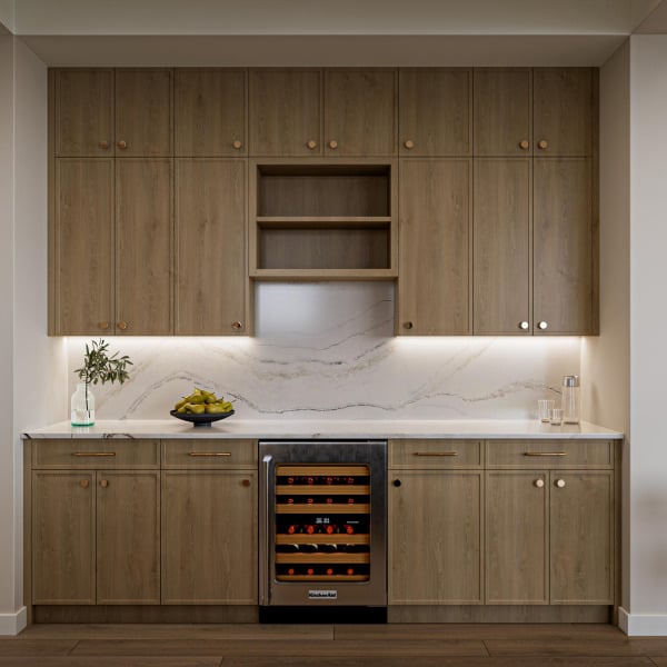 Modern kitchen with light wood cabinets, marble backsplash, under-cabinet lighting, and a wine cooler.